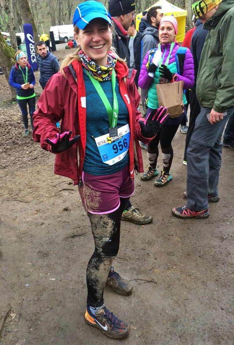 Writer Jennifer Hattam stands on a muddy trail after finishing a race in Istanbul. She's wearing a running bib and her clothes caked in mud 