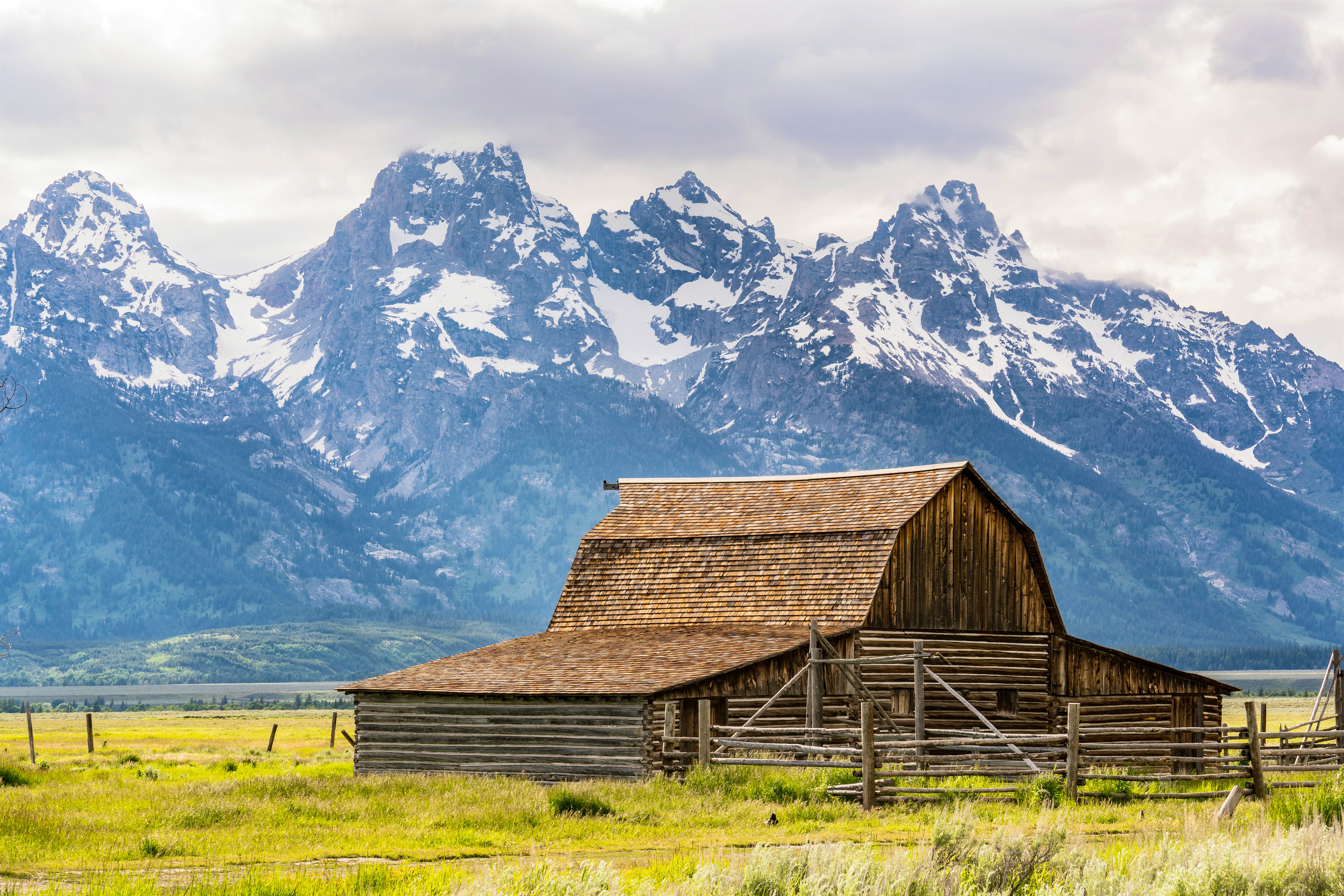 A weathered barn with snowcapped mountains in the background