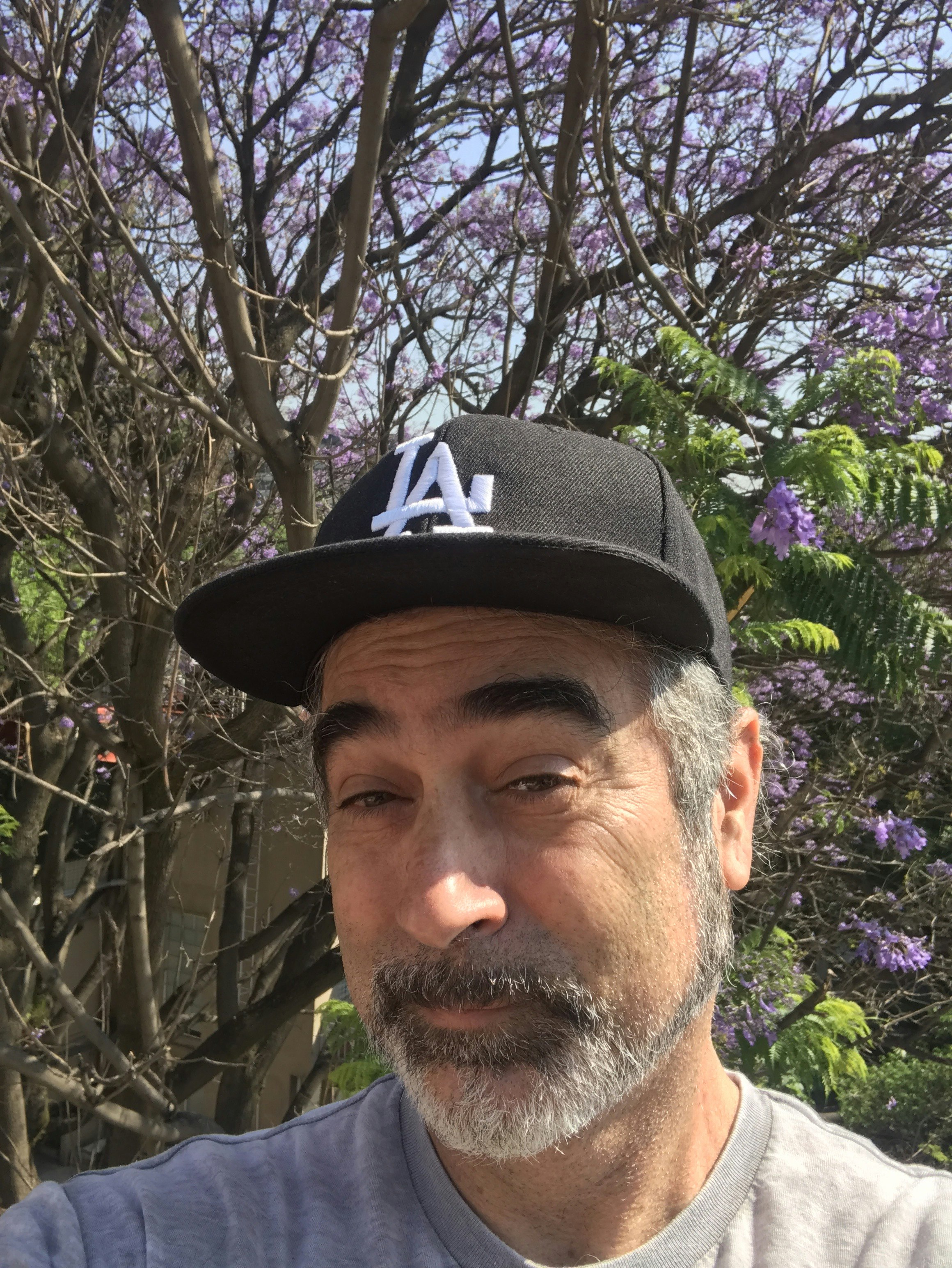 A man in a baseball cap in front of a flowering tree