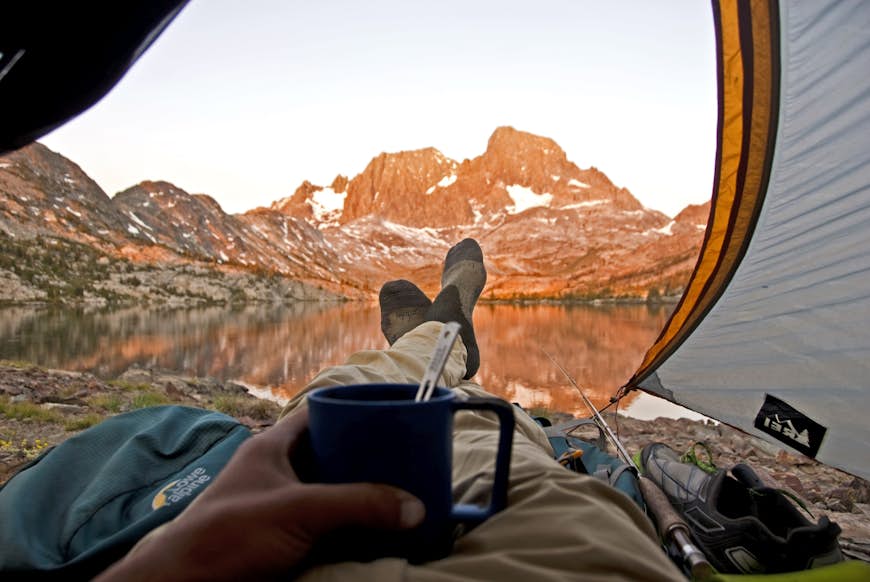 Ser man ut genom entrén till ett tält med bergen i Sierra Nevada i fjärran, står en mans fötter och en kopp soppa i balans på magen.