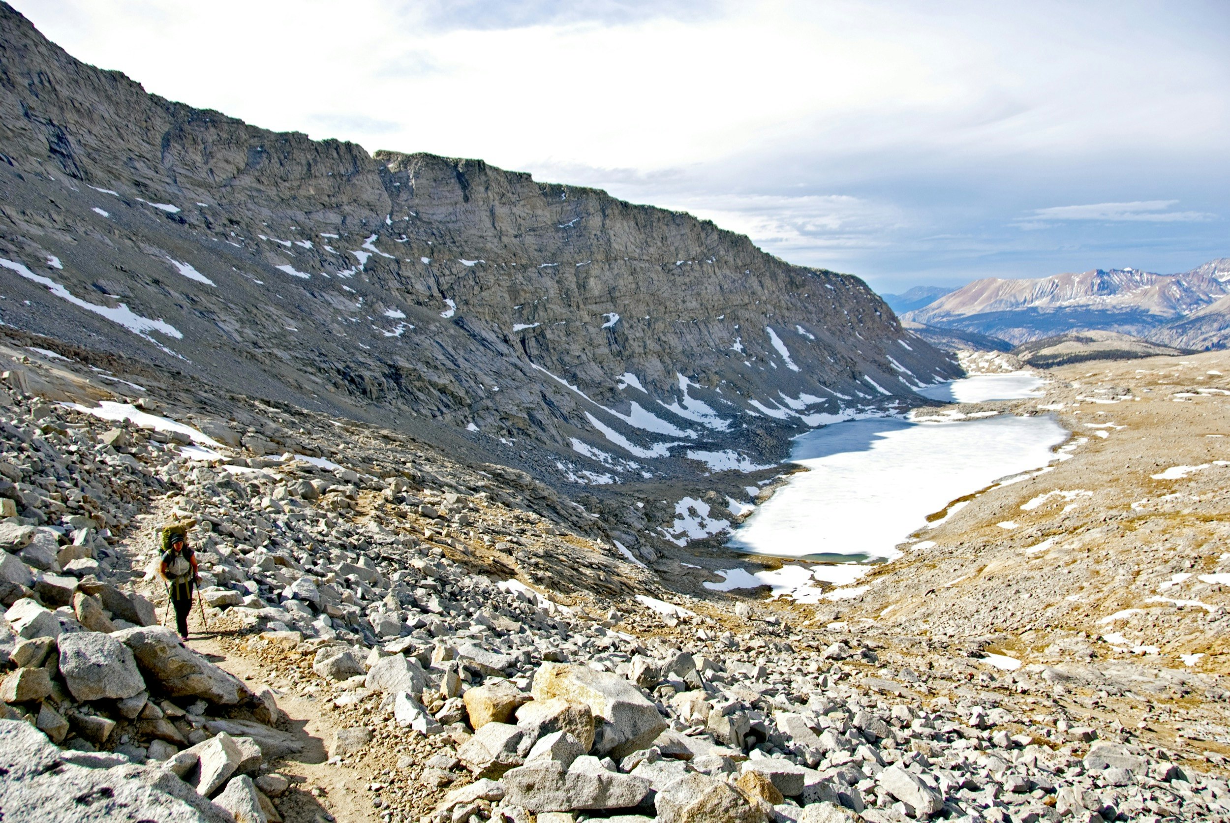 A man walks through a rocky landscape on the John Muir Trail in California's Sierra Nevada among patches of snow
