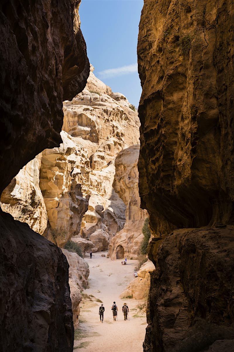 Three hikers walk through a narrow, rocky gorge that towers above them.