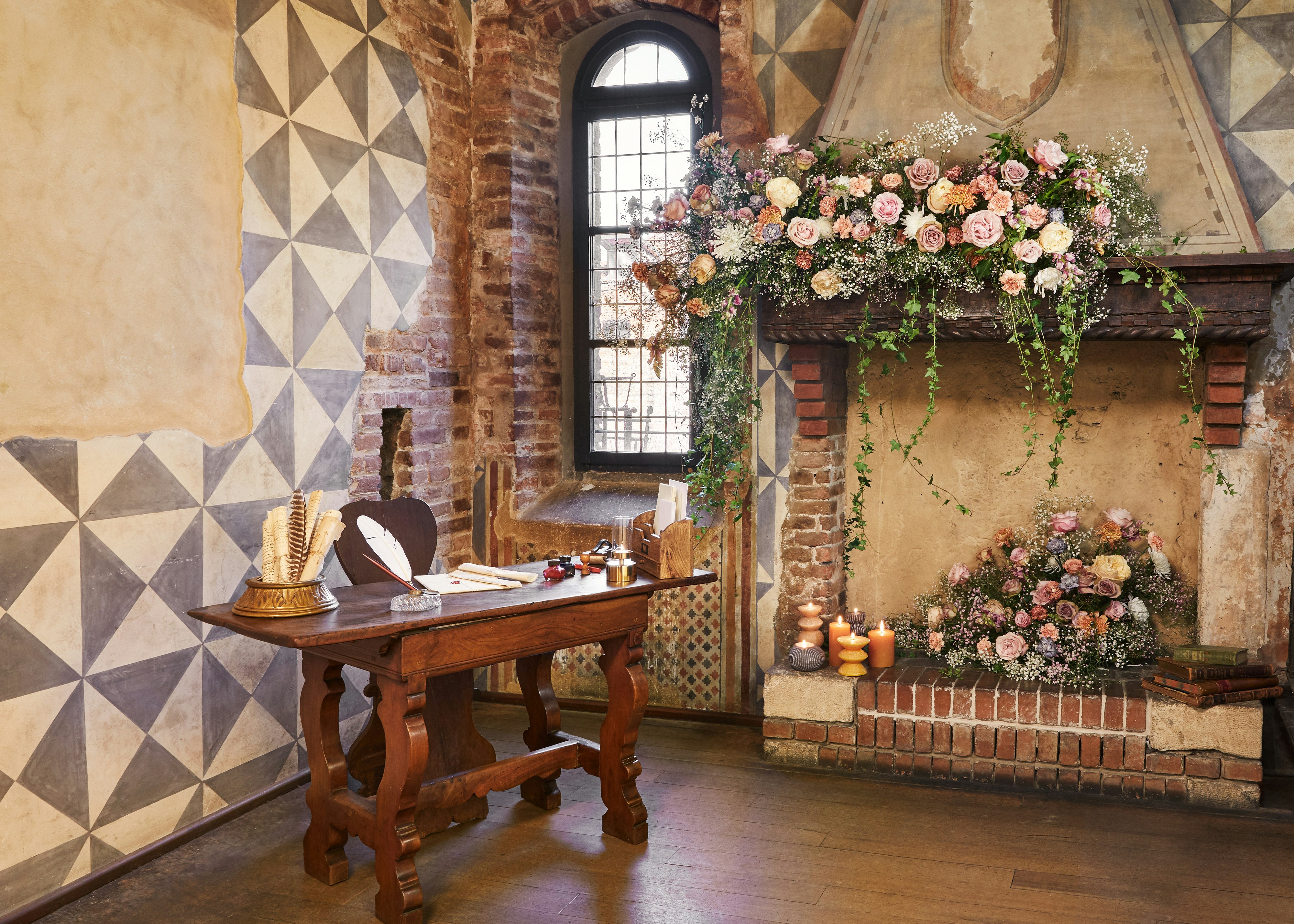 A wooden writing desk beside a flower-covered stone fireplace
