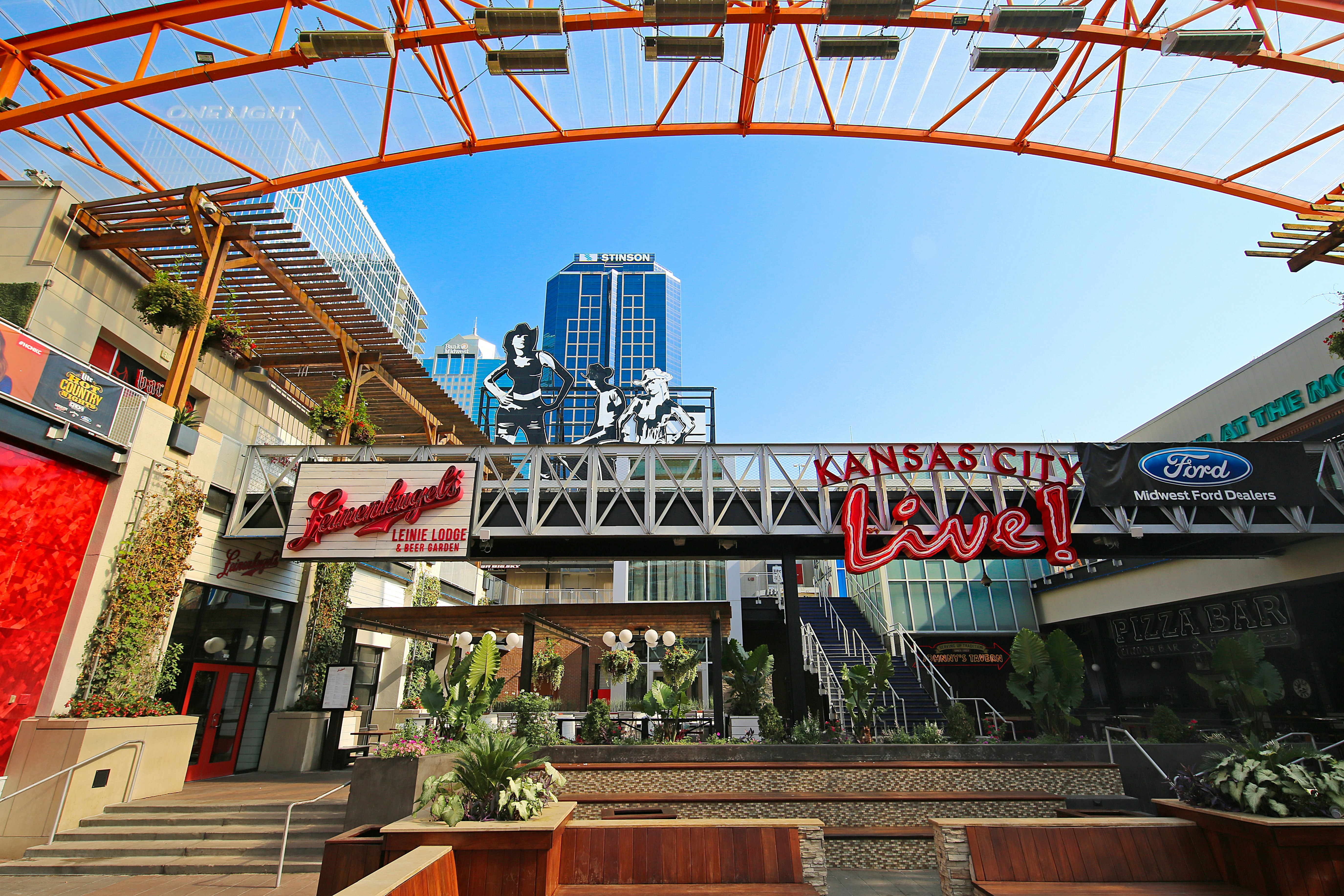 Red and white neon signs hang on rafters at Kansas City Live. The courtyard is filled with outdoor seating and plants. 