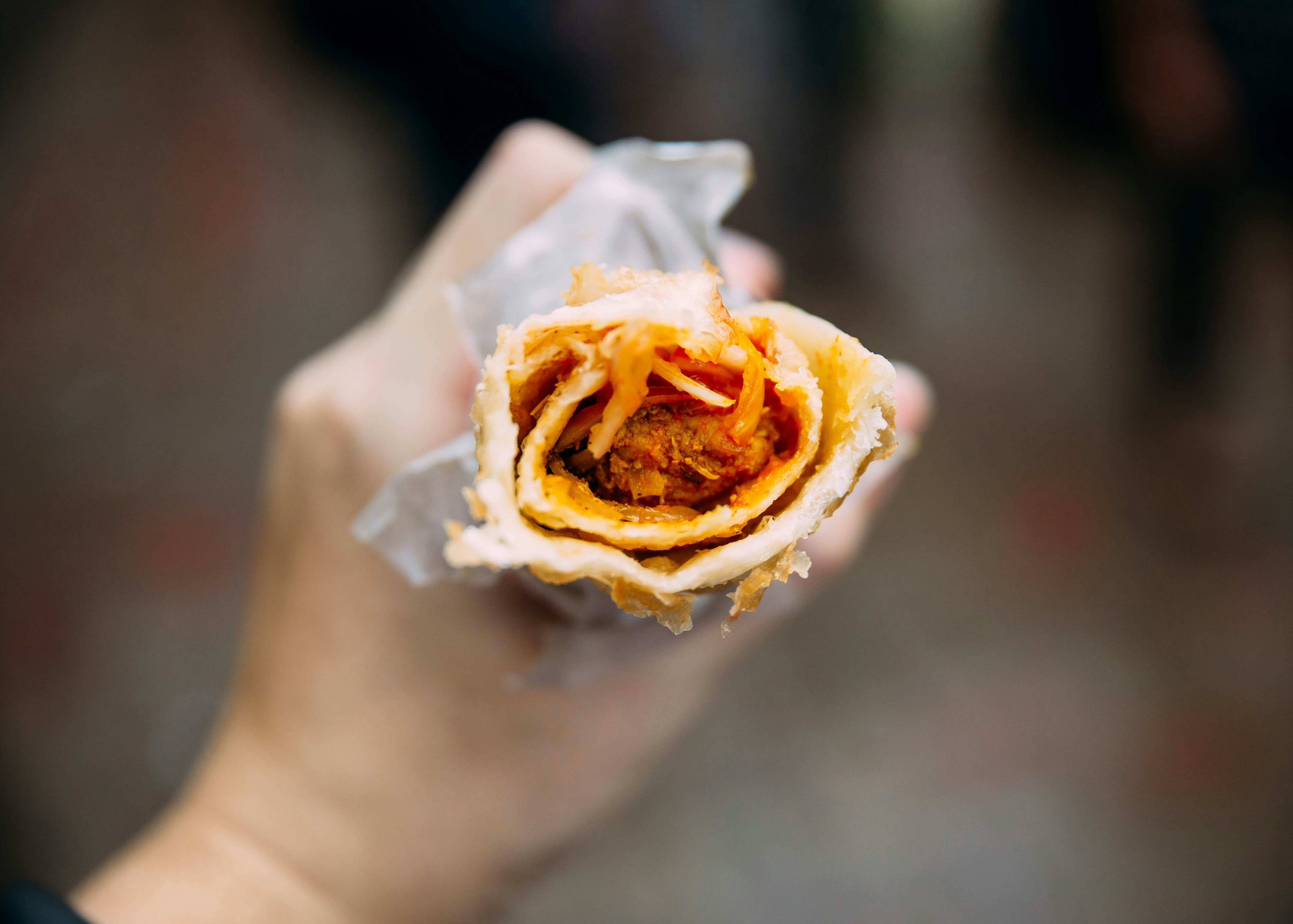 A meat kati roll being gripped by a person's hand, with the open end pointing directly towards the camera. Inside the roll the meat filling is visible.