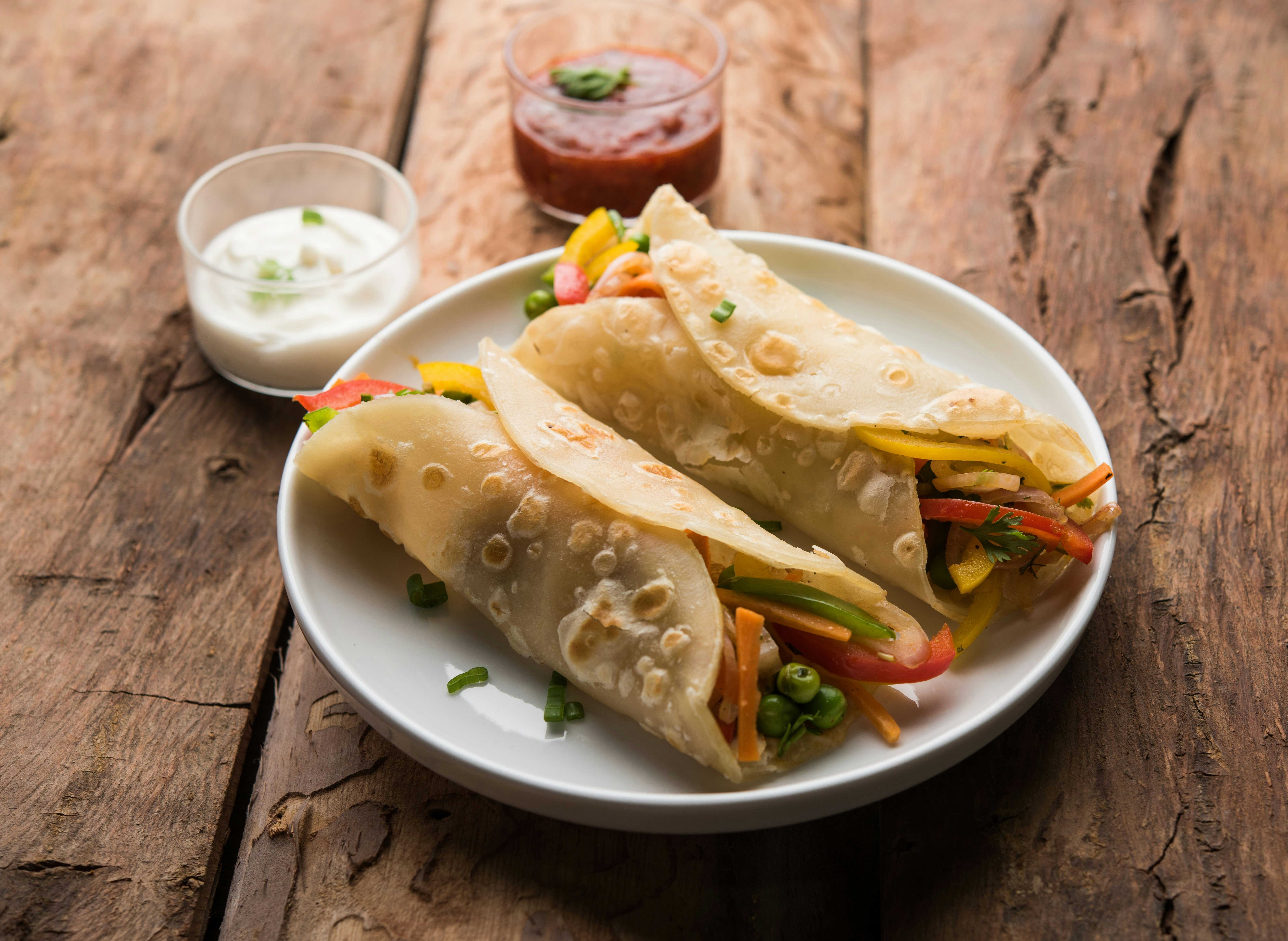 Two kati rolls are displayed on a plate; colourful vegetables are spilling out of the wraps.