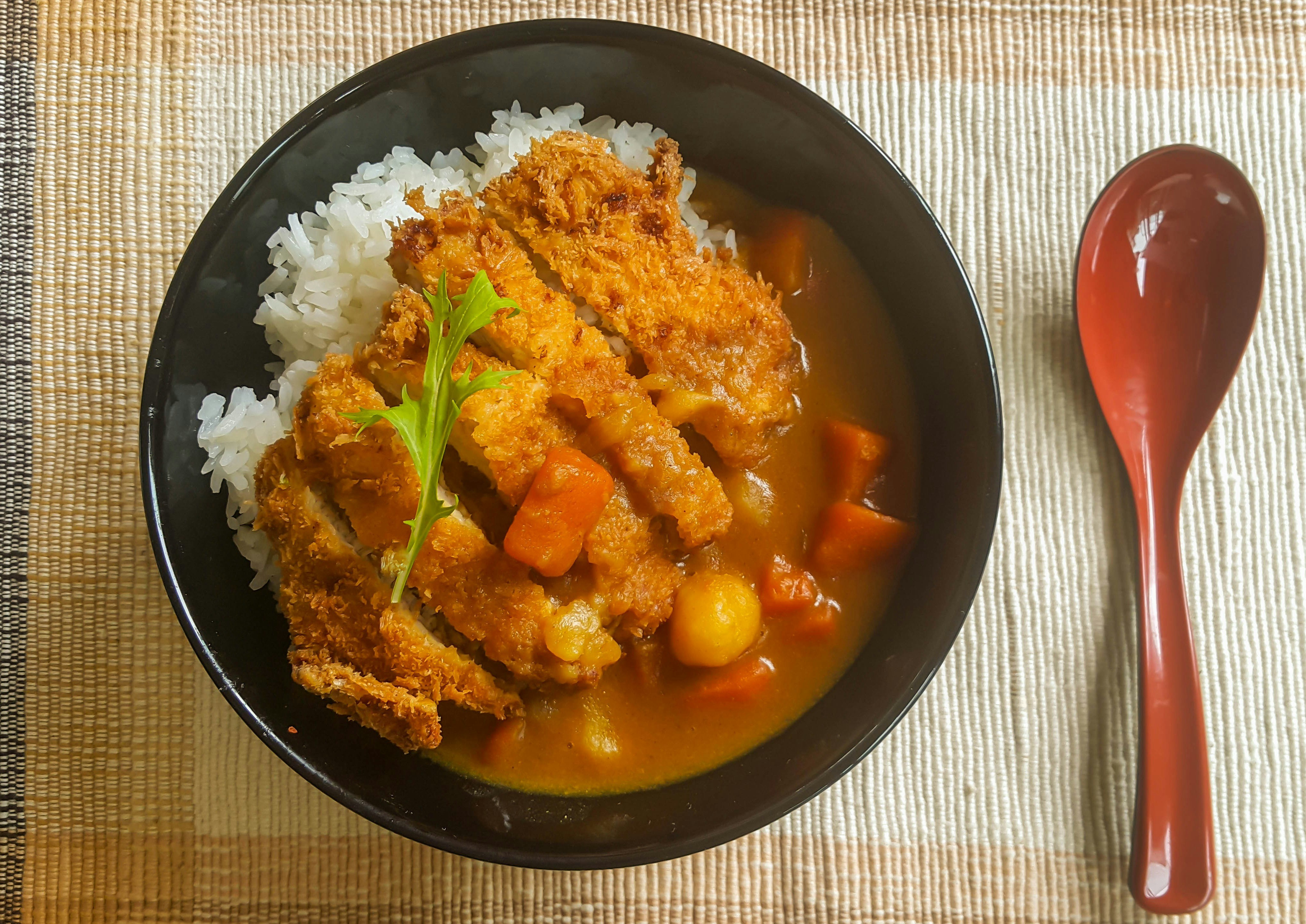 A top-down view of a plate of katsu curry: a Japanese dish consisting of meat in breadcrumbs, rice and a thick curry sauce.