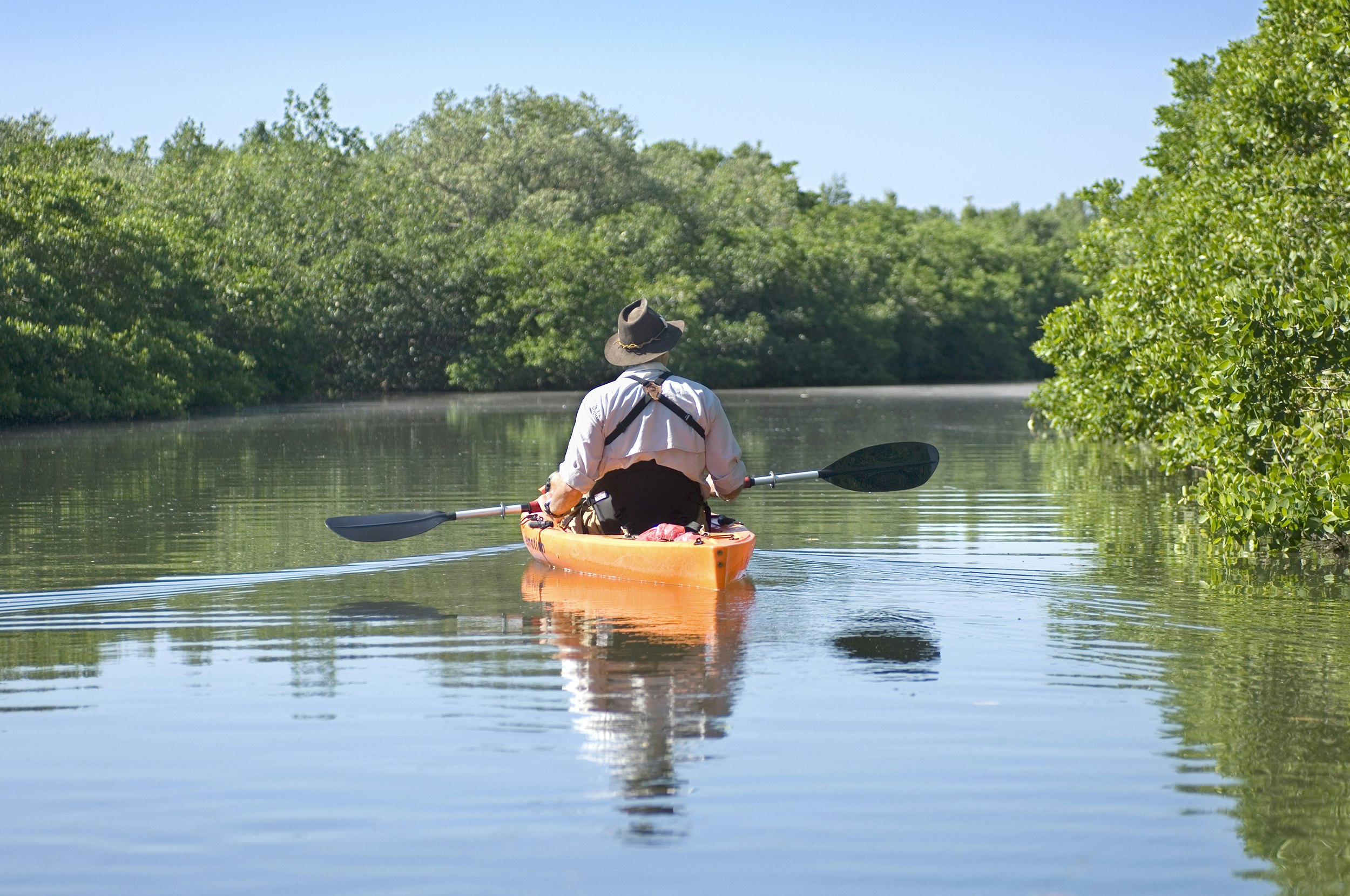A man in an orange kayak paddling the still waters of Fort De Soto Park in Florida