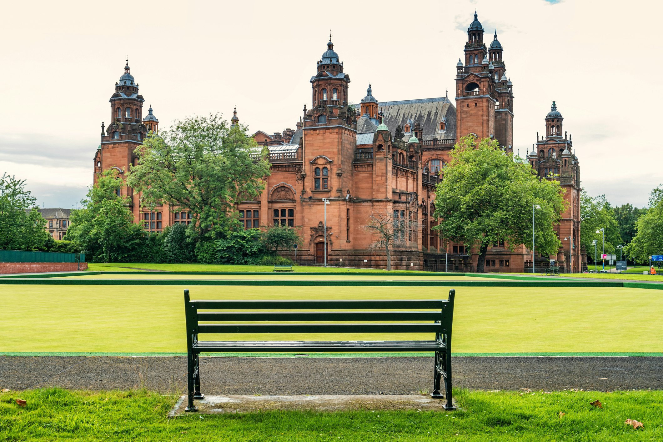 Glasgow's Kelvingrove Art Gallery, a beautiful baroque building on a sprawling green lawn from the vantage point of a park bench.