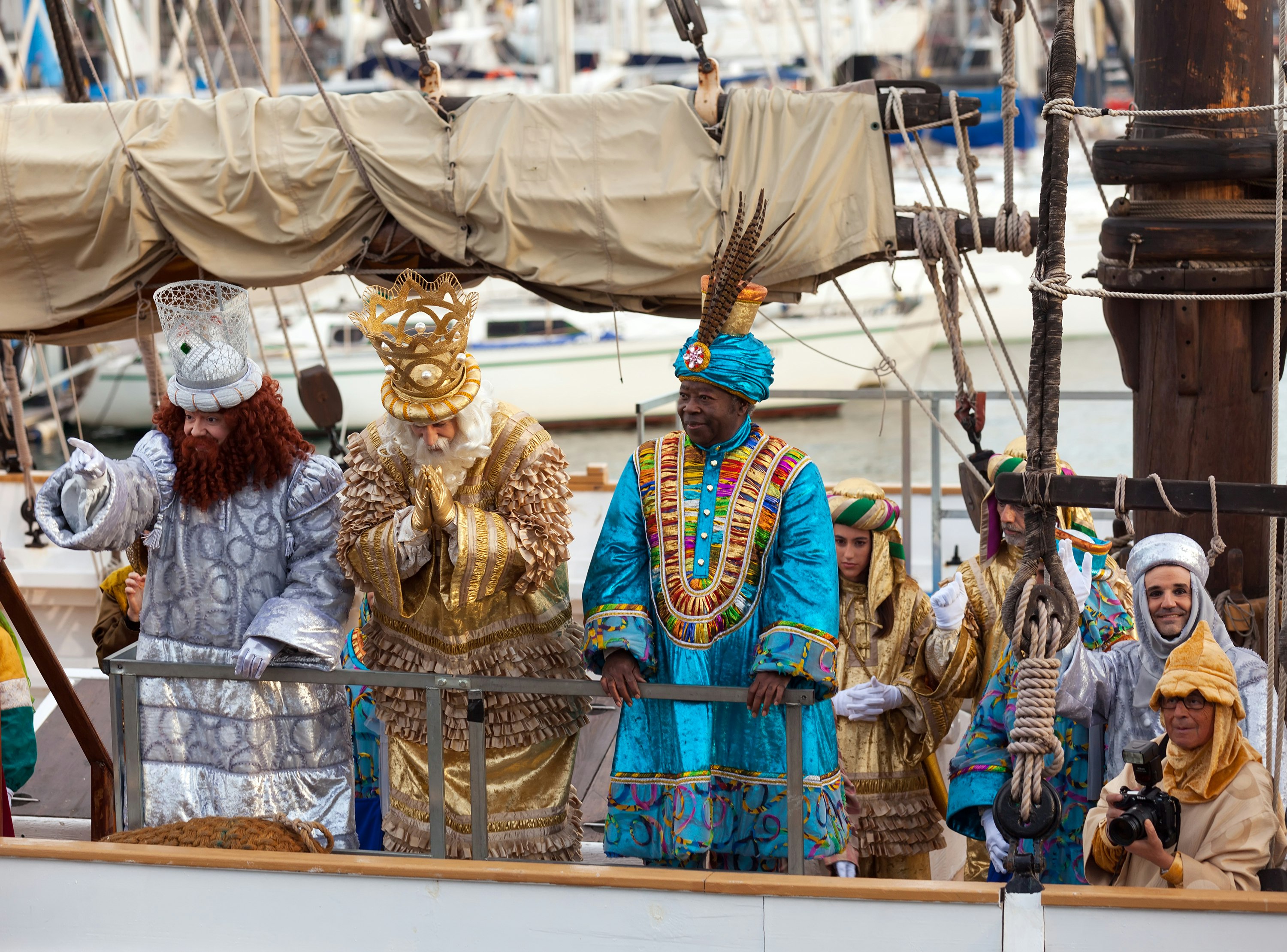Men dressed as the Three Kings in elaborate outfits stand on a boat on Kings Day in Barcelona, with their subjects behind them.