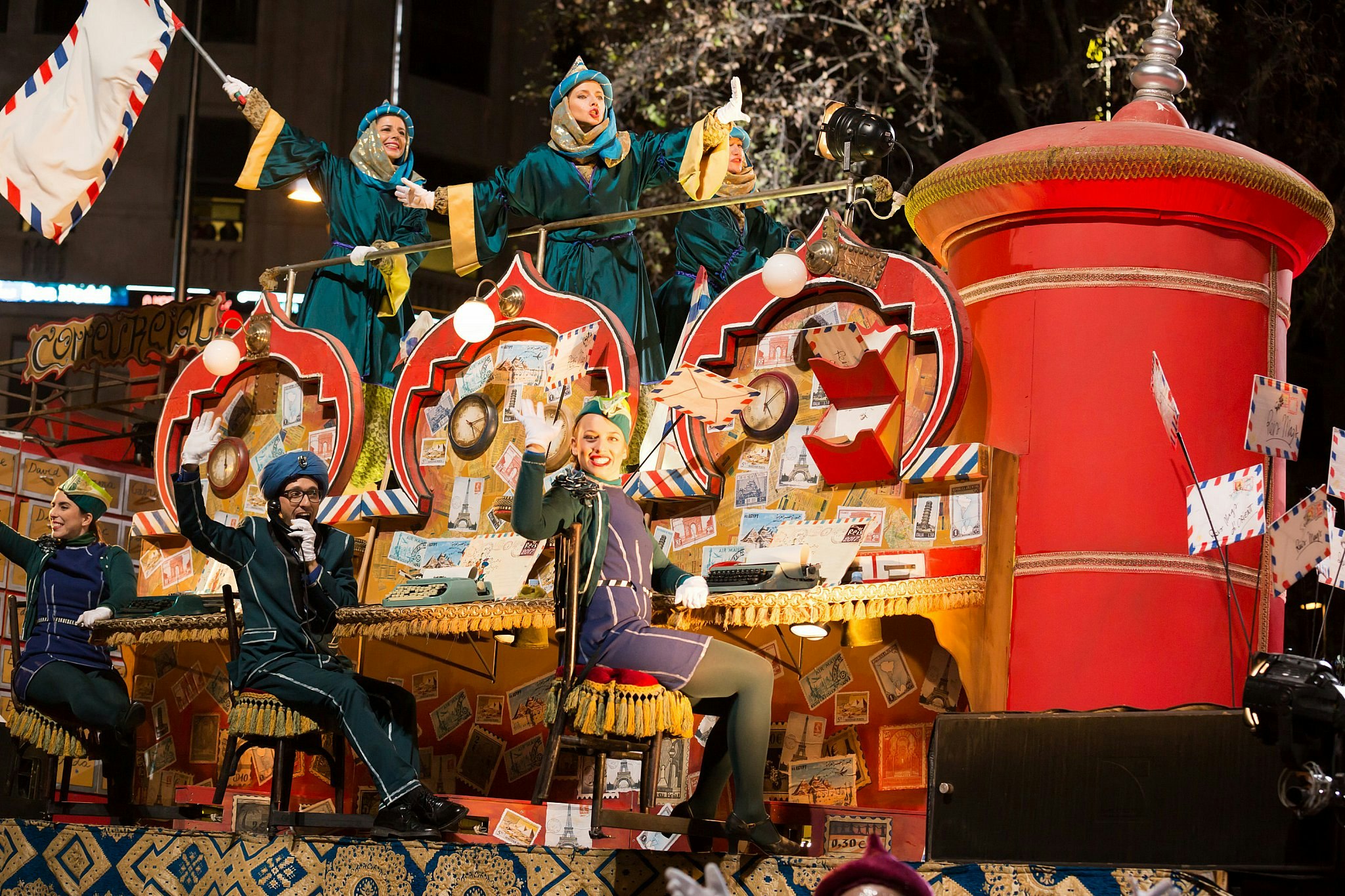 The Kings' Day parade in Barcelona: people are on a float dressed in blue outfits, sitting at desks with vintage typewriters and airmail letters.
