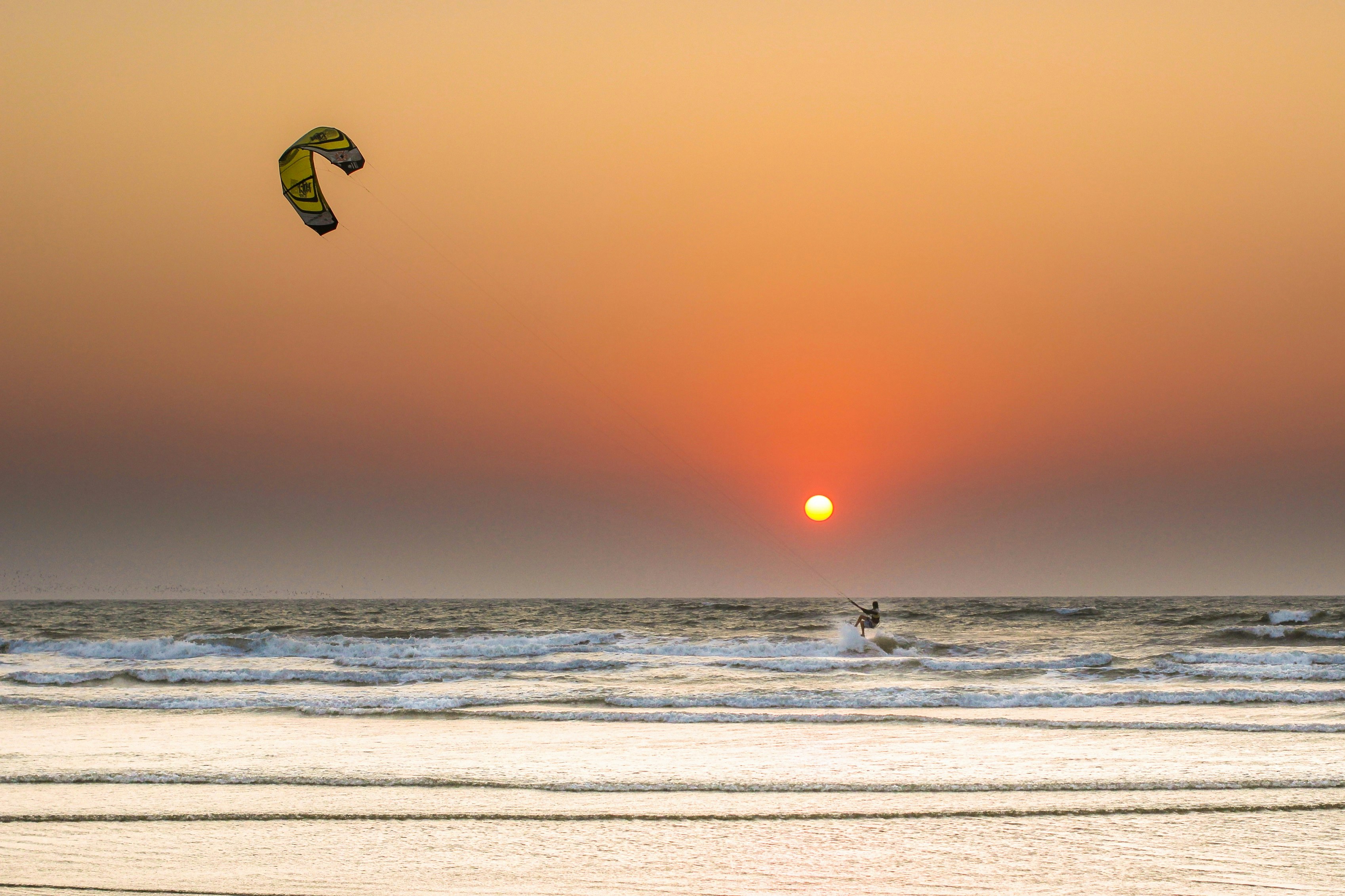 A kite surfer in the waves in front of an orange sunset