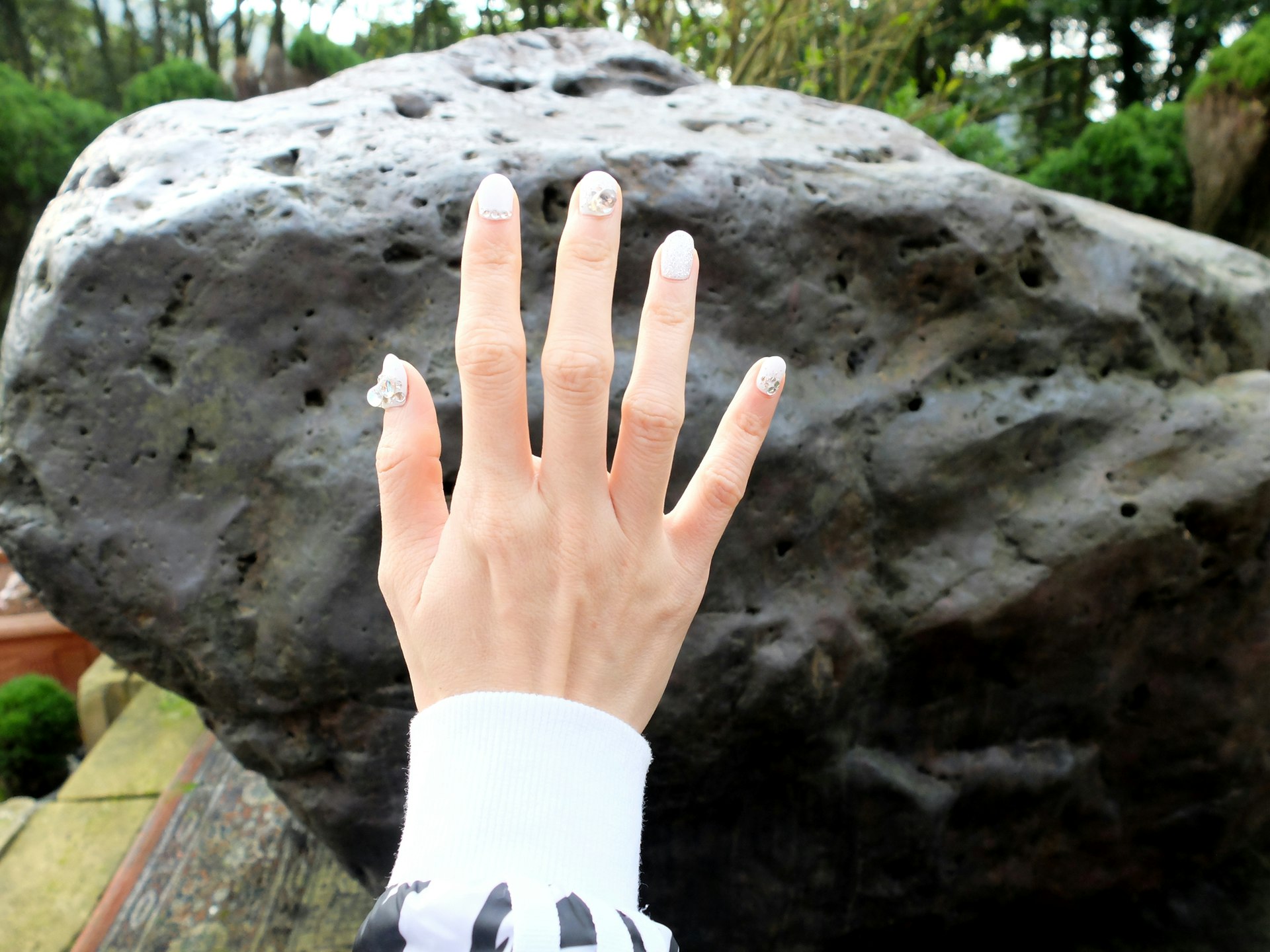 A female hand is held up in front of a large black boulder that is claimed to be a meteorite full of chi.