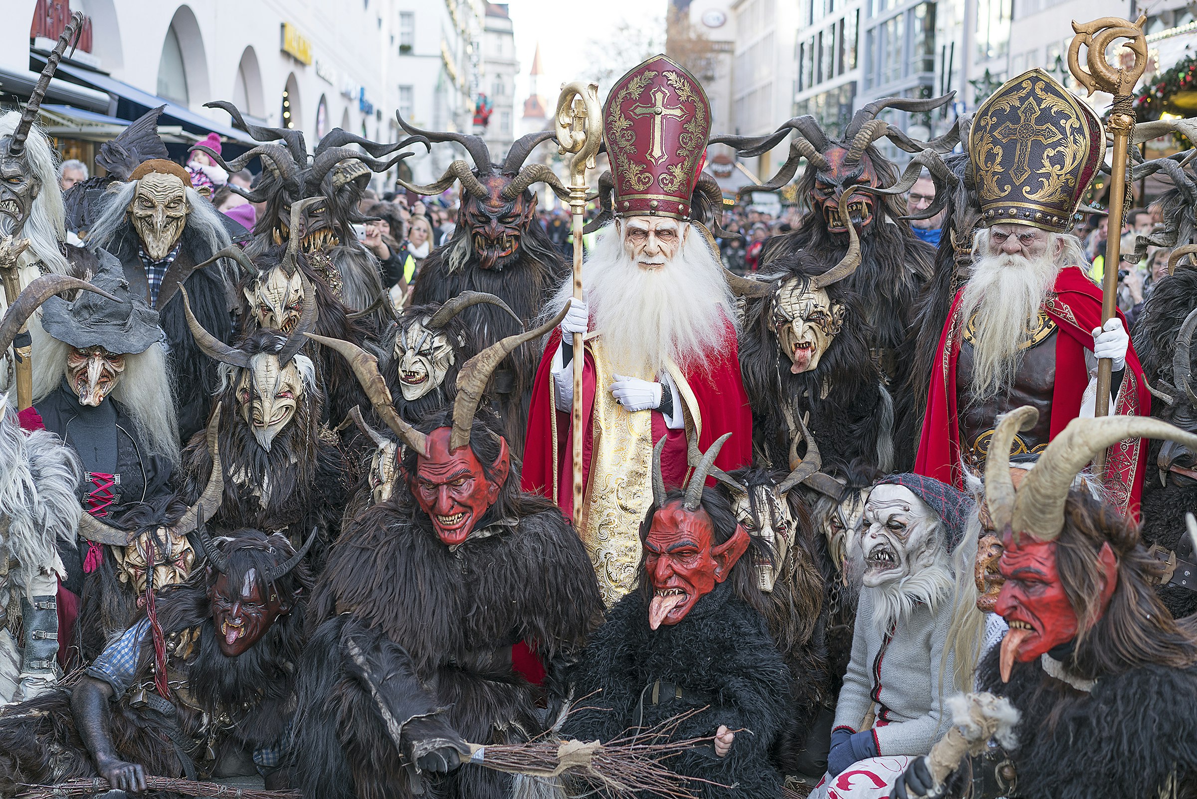 A group of people dressed in different styles of Krampus costumes pose for the camera on a Munich street.