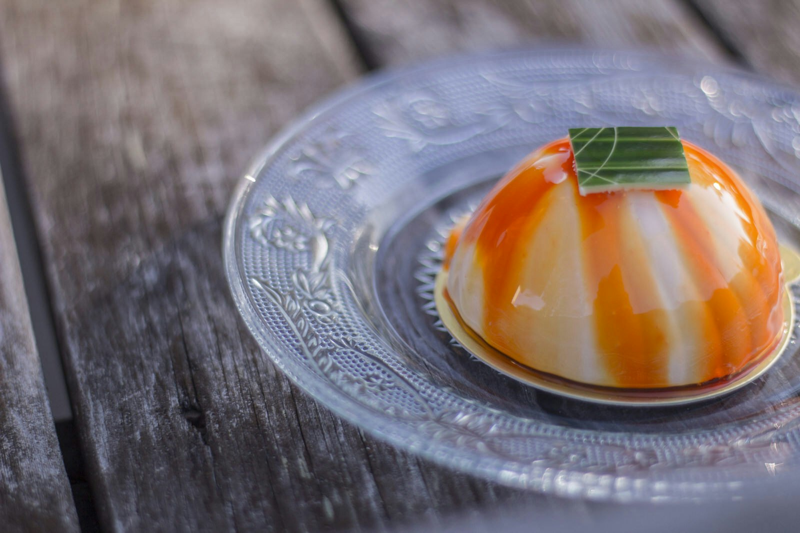 A domed, gelatin dessert with orange marbling served on an intricately patterned glass dish.