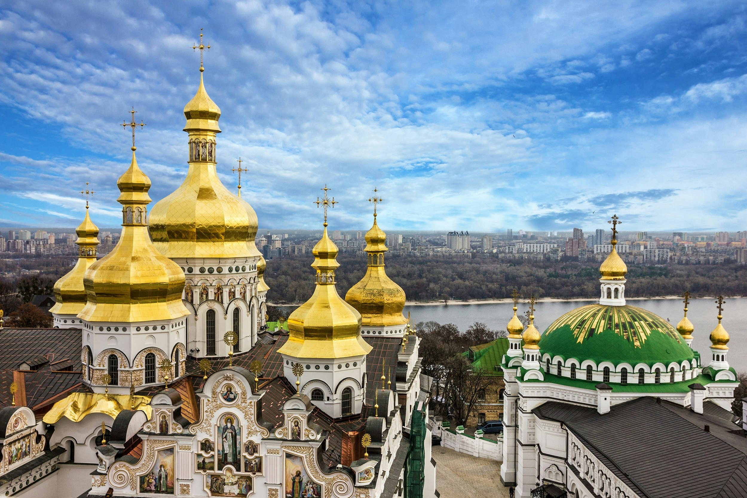 Five golden domes and one larger, flatter green dome, with a view beyond to a river at Kyevo-Pecherska Lavra in Kiev