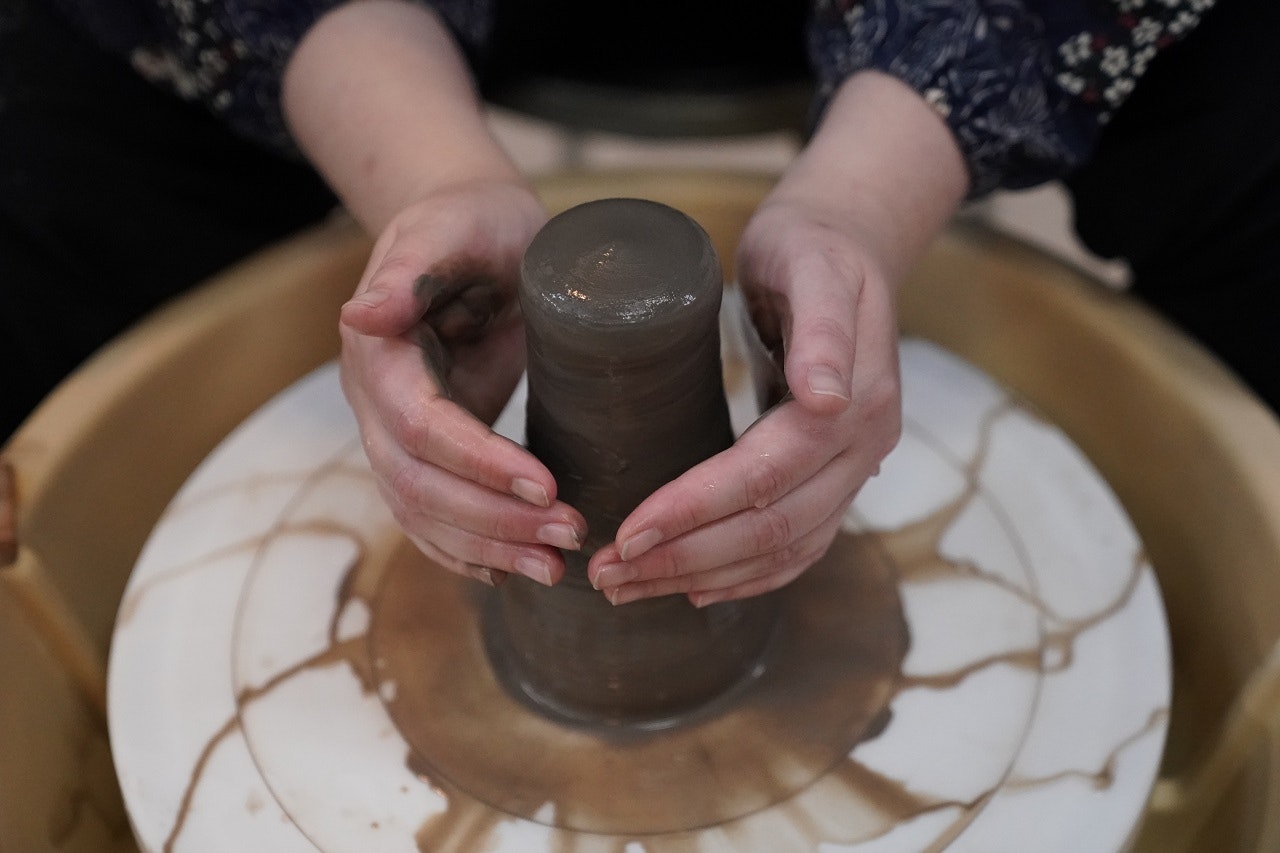 A woman moulds a vase on a pottery wheel