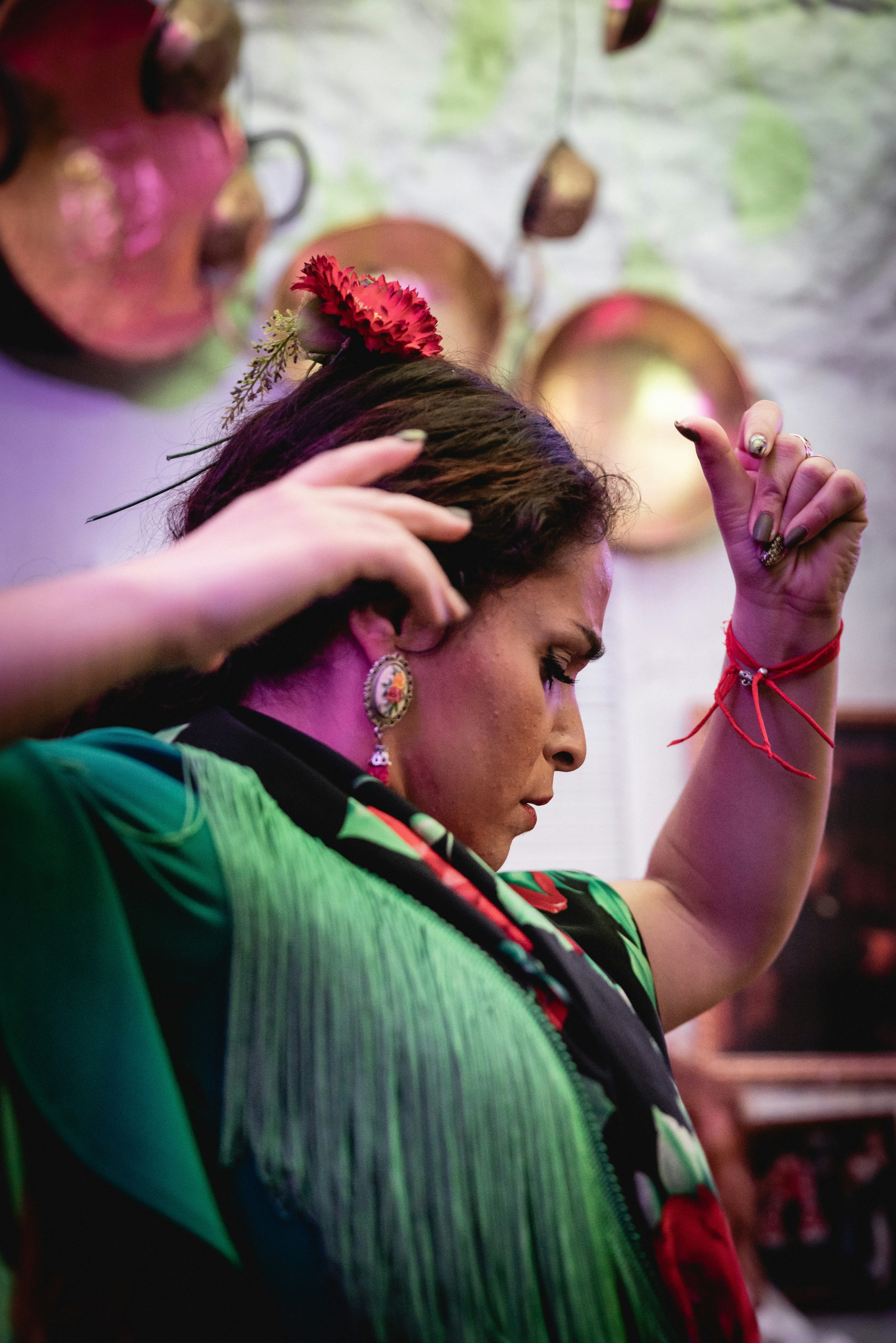 A close-up photo of a woman dancing Flamenco. She is wearing a jade green top; her arms are held aloft and she is looking downwards. 