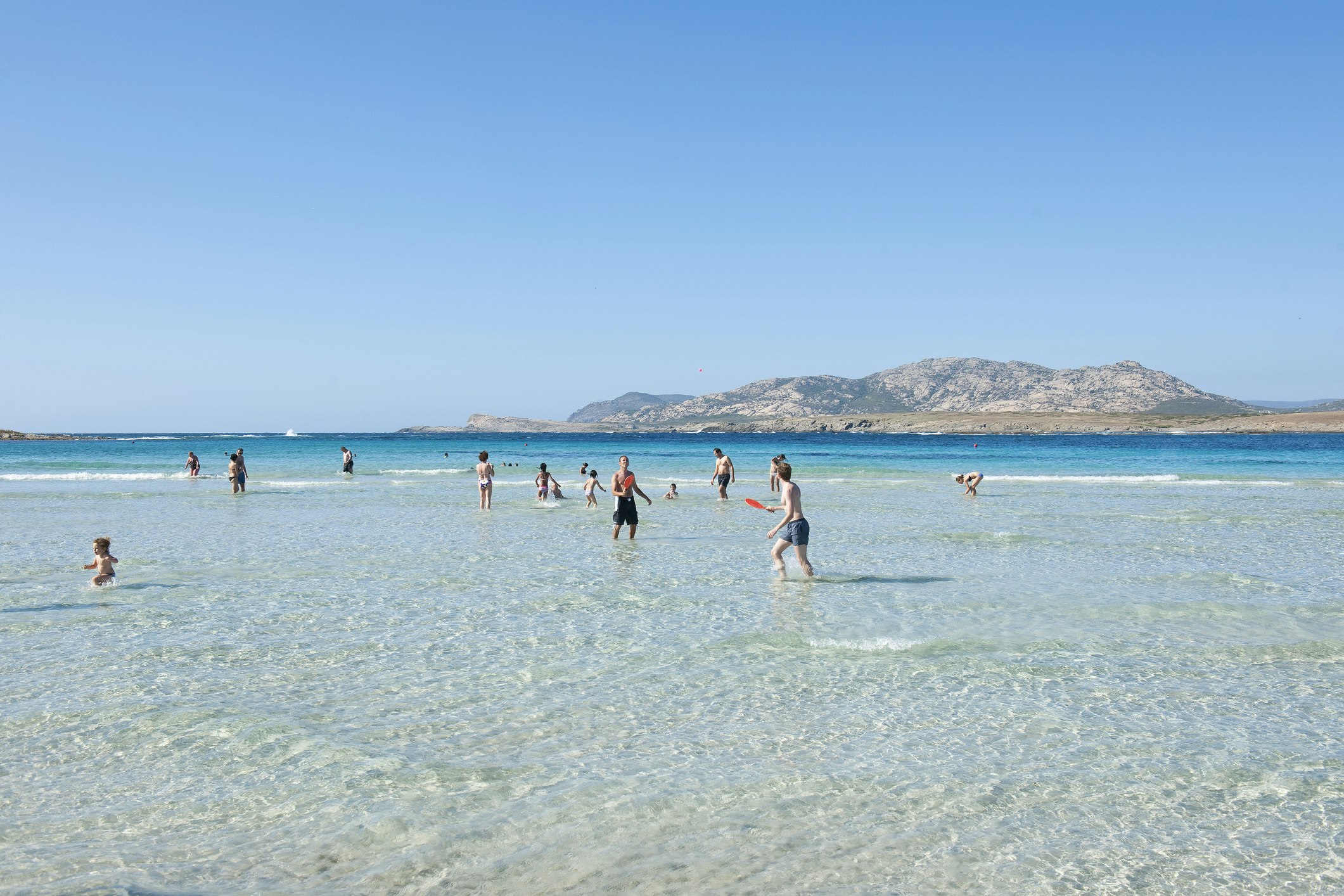 Holidaymakers play in the clear waters of La Pelosa Beach