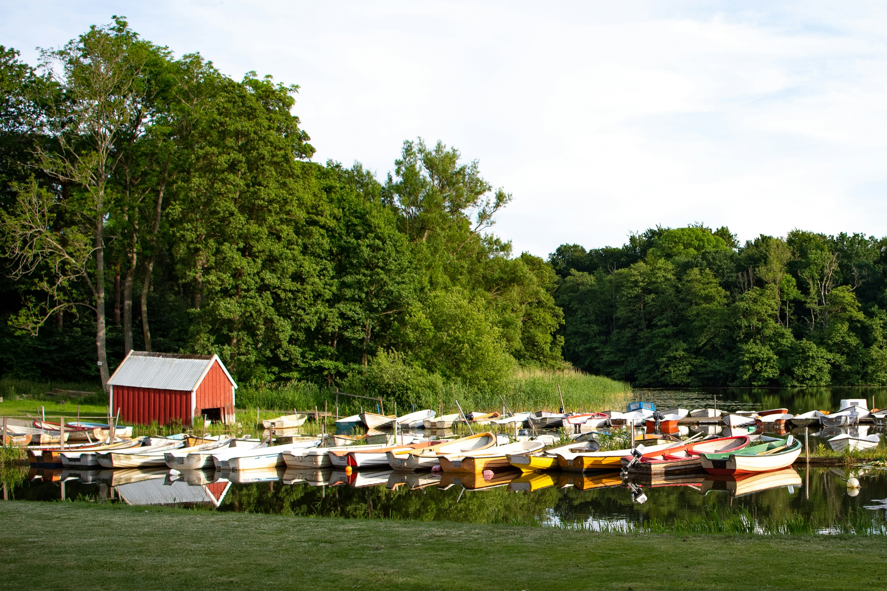 Rows of colorful rowboats and other watercraft sit next to a red shed on the shores of Lake Sövde in Skåne, Sweden
