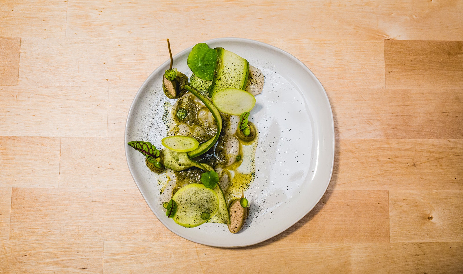 An overhead view of a white plate artfully filled with zucchini and other vegetables covered in spices and leafy garnishes. Las Puertas, Buffalo, NY.