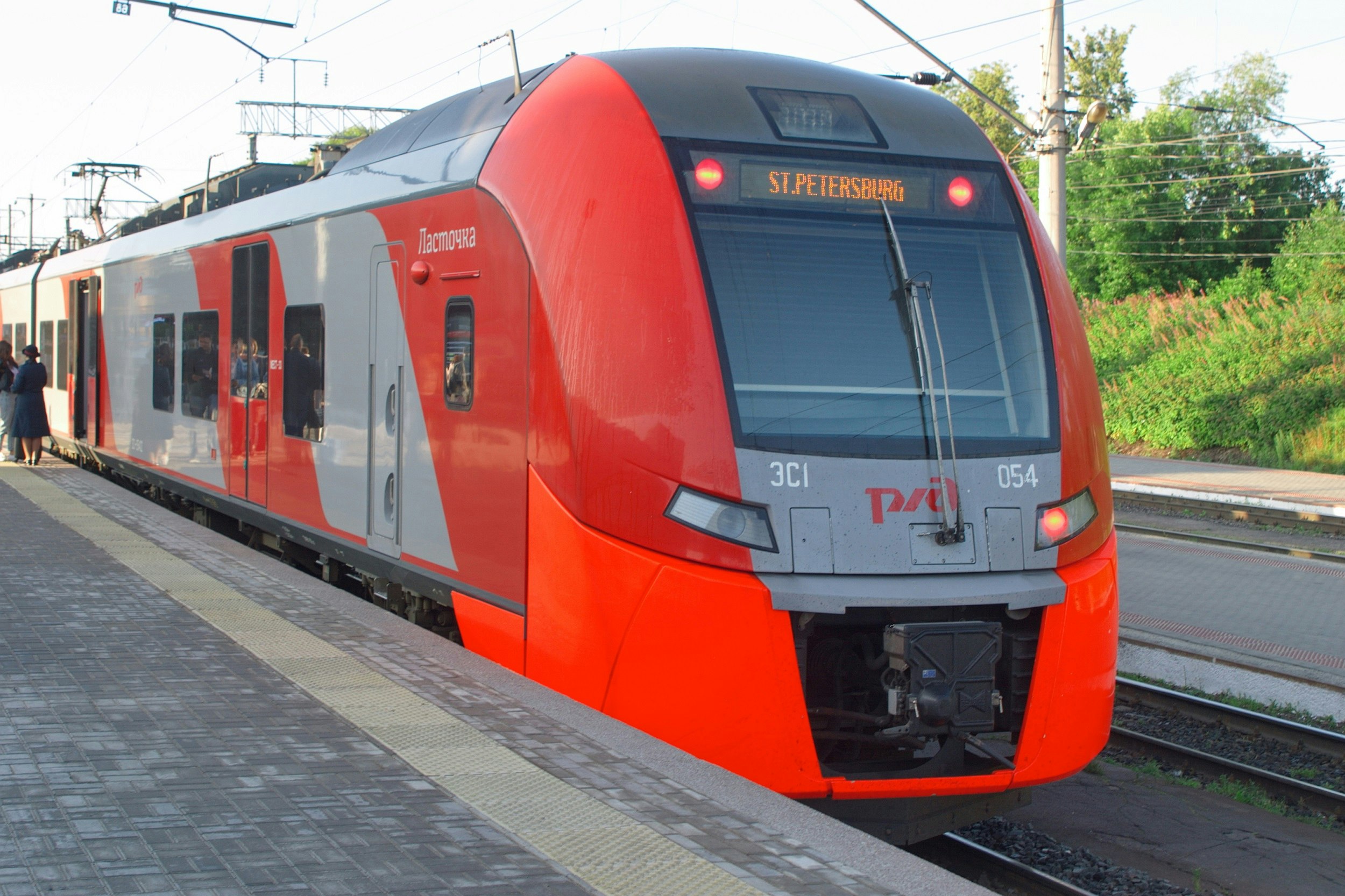 The front of a red-and-grey train waiting at a platform. The electronic sign at the front of the train says 'St Petersburg'