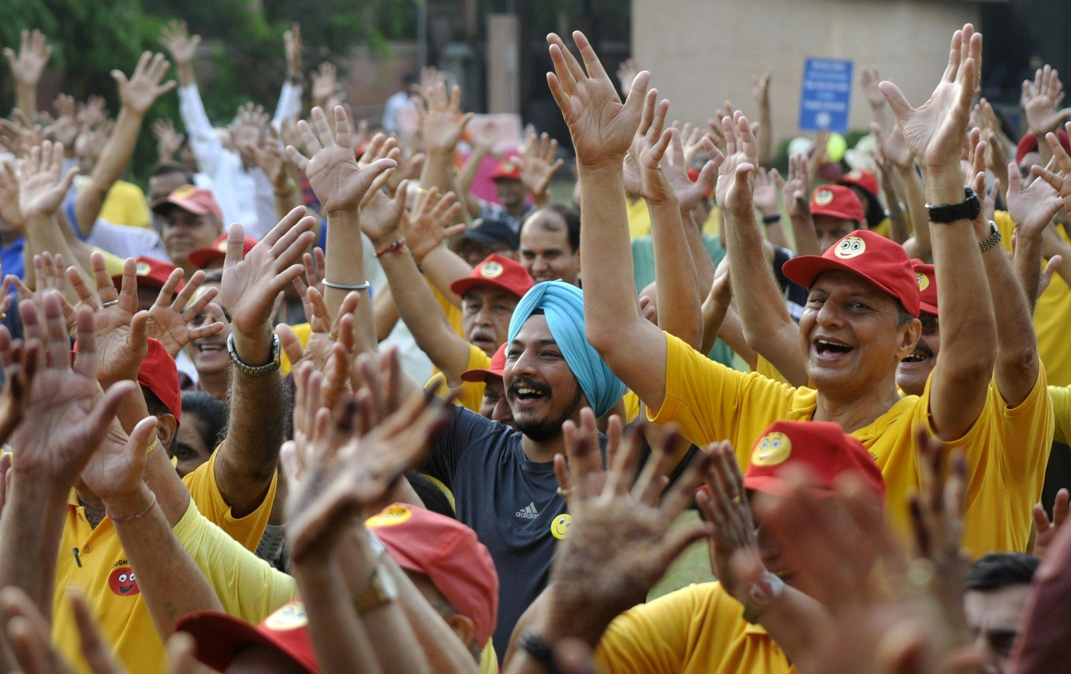 A large group of people raise their hands in the air and laugh during a laughter yoga class in India.