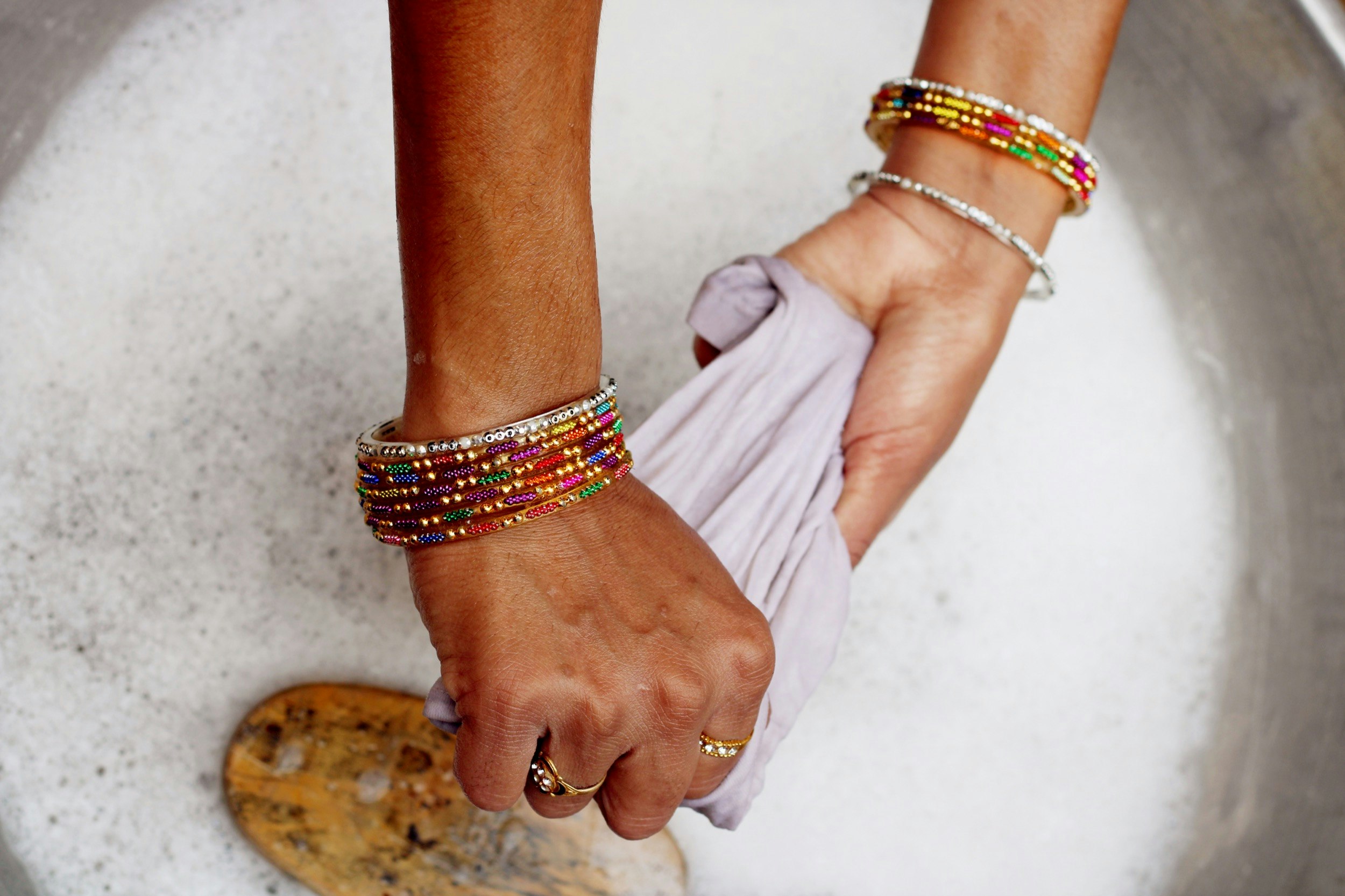 A woman's hands are shown wringing soapy water out of clothes in a white sink; Upping your travel game