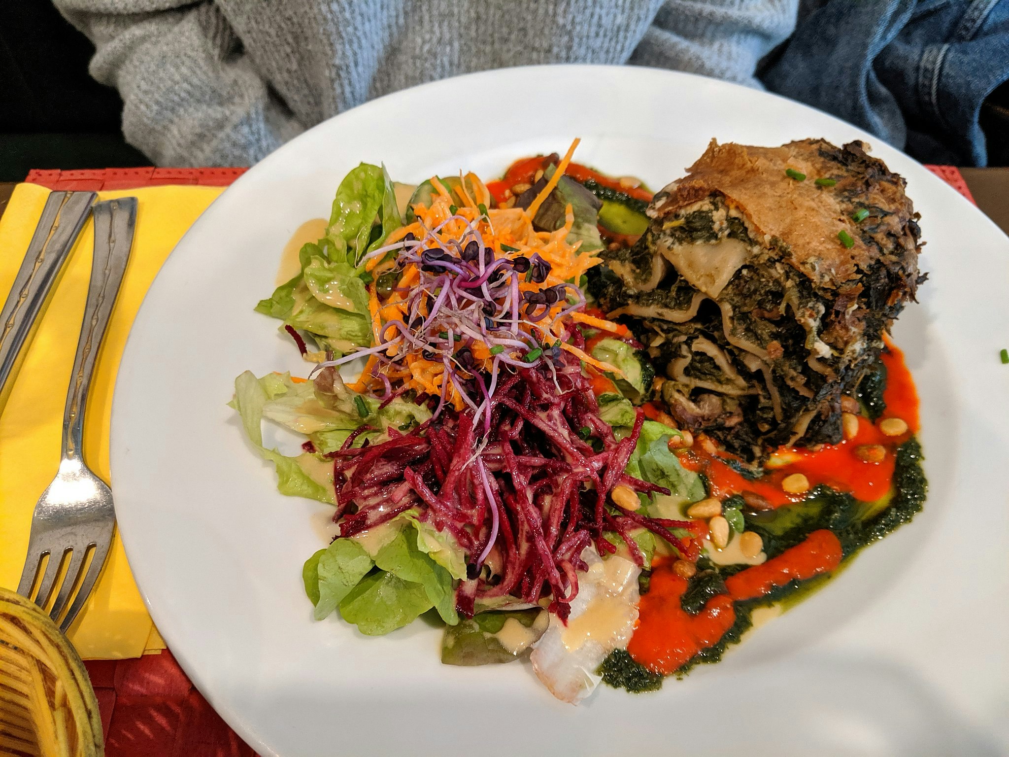 A veggie lasagne on a white plate with a colourful salad.