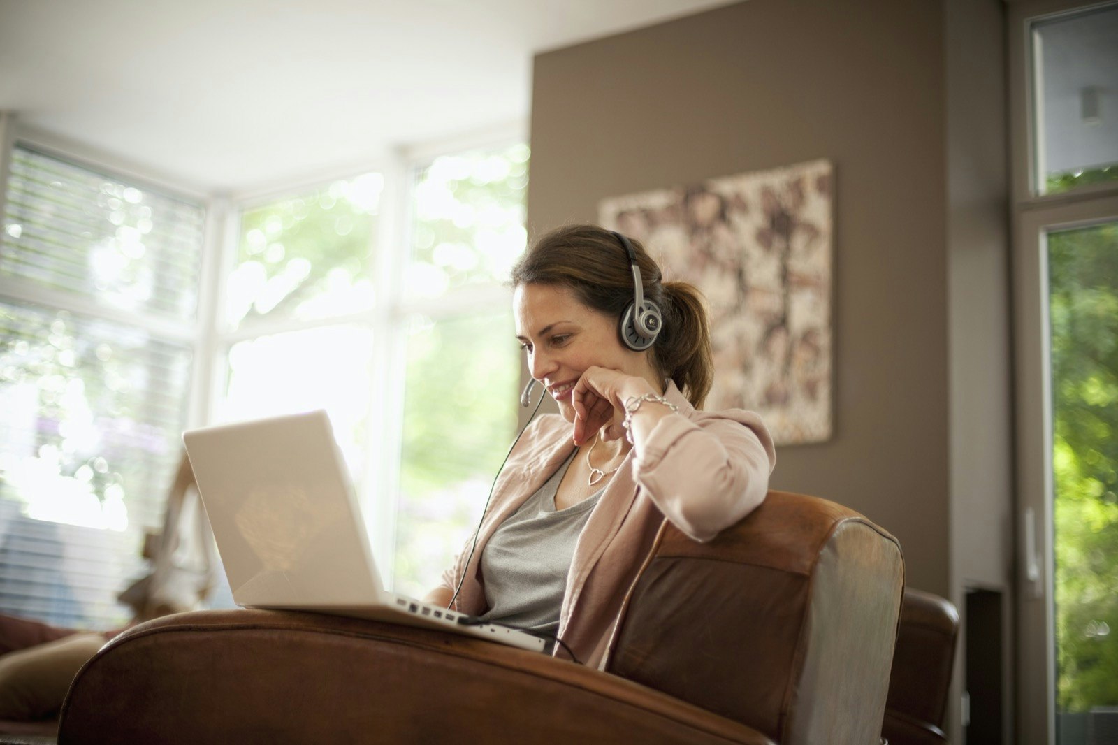 A woman uses headphones with a microphone as she sits alone with a laptop