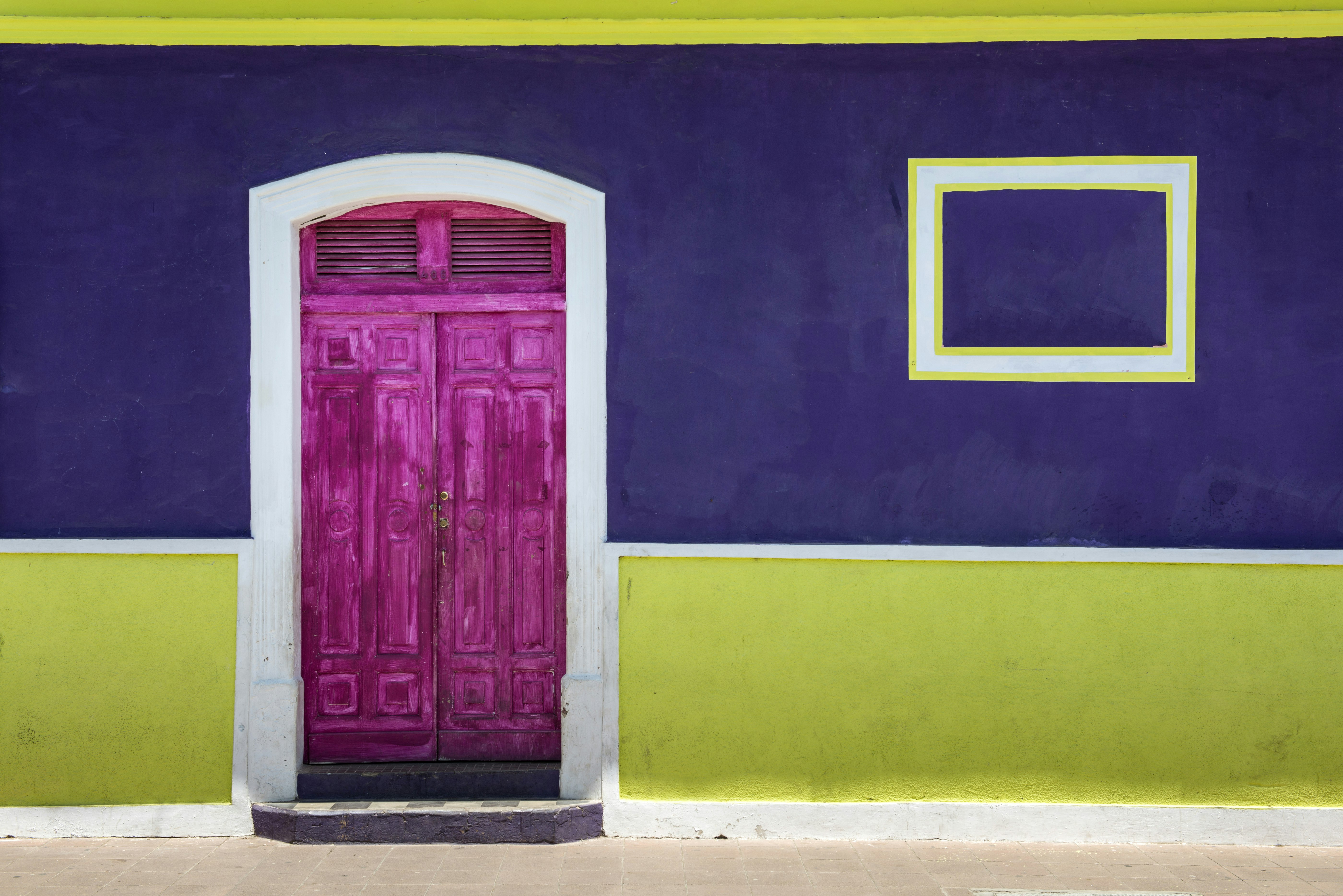 A bright pink door with a white border clashes with the blue, white and light green exterior of a house in Leon, Nicaragua 