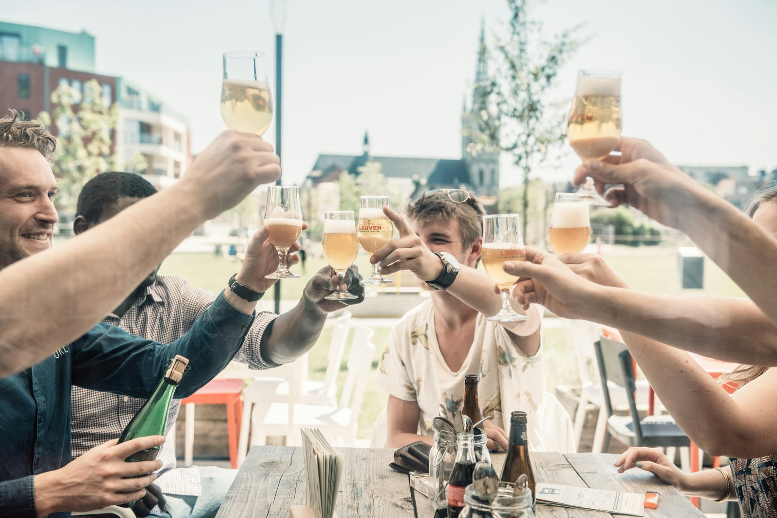 Several people sitting around a wooden picnic table in Leuven, Belgium, doing a cheers with beer glasses