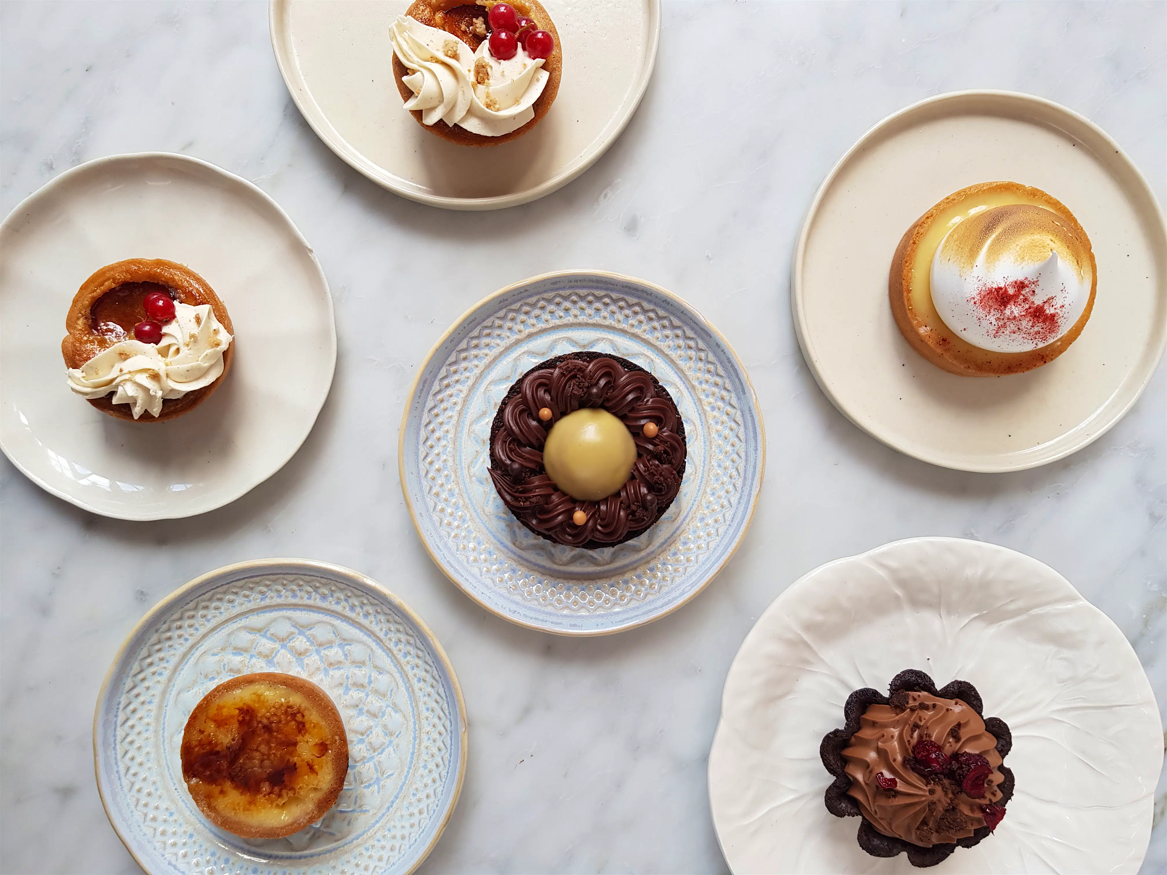 Lily Vanilli Assorted colourful pastries displayed on white plates set on a white marble surface at Lily Vanilli in east London.