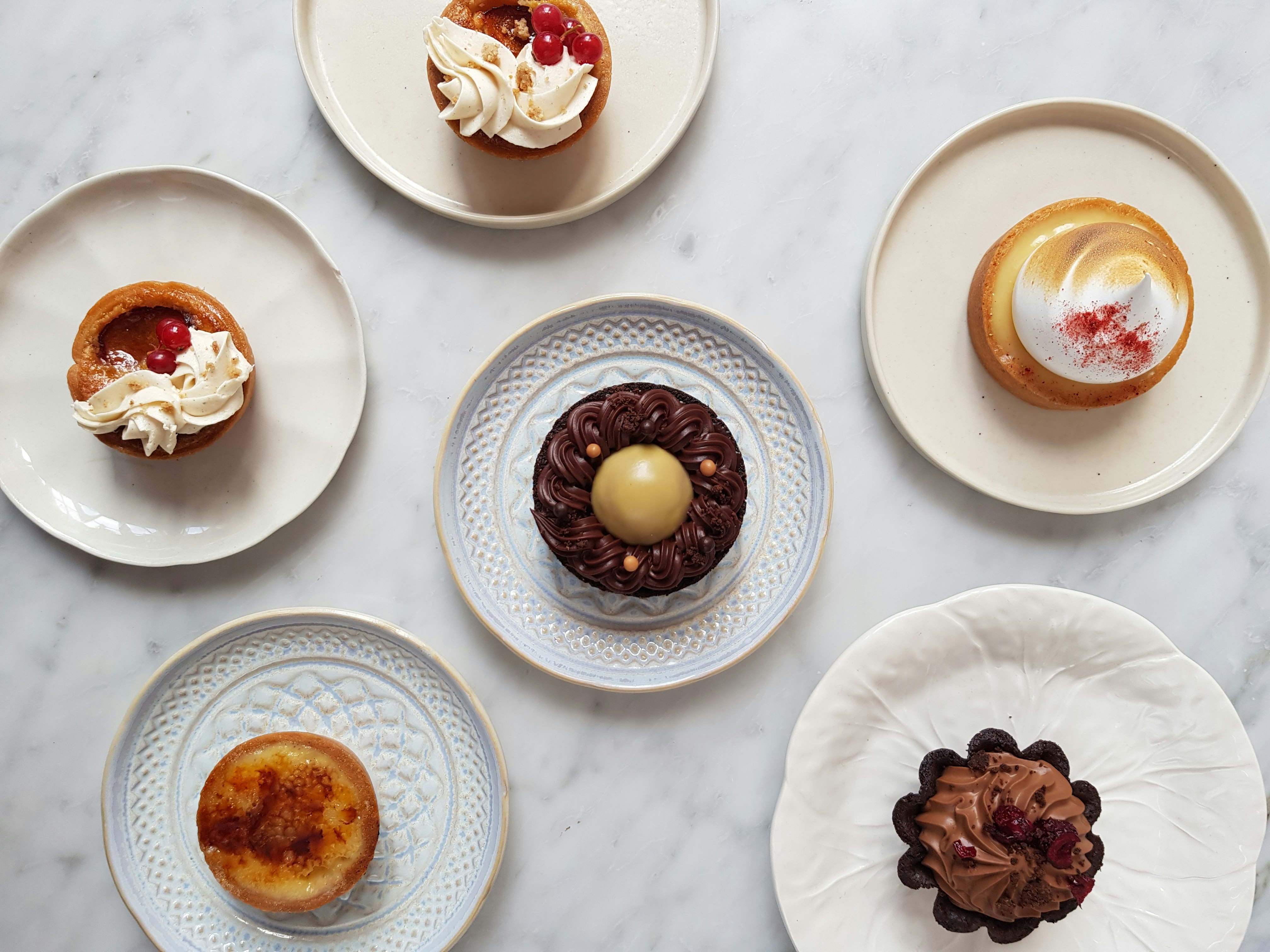 Assorted colourful pastries displayed on white plates set on a white marble surface at Lily Vanilli in east London.
