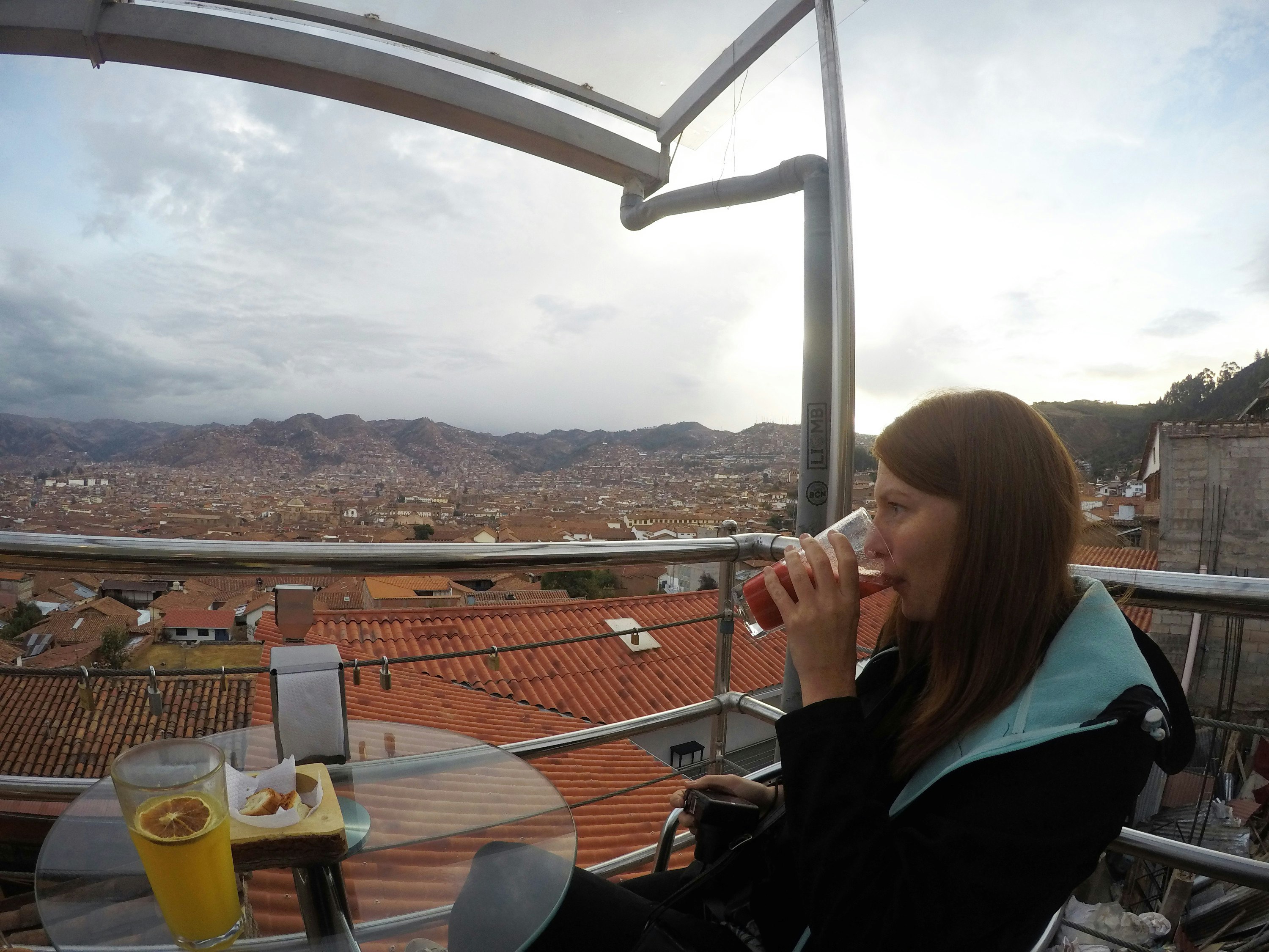 A woman sits sipping a juice on a rooftop terrace overlooking Cuzco.