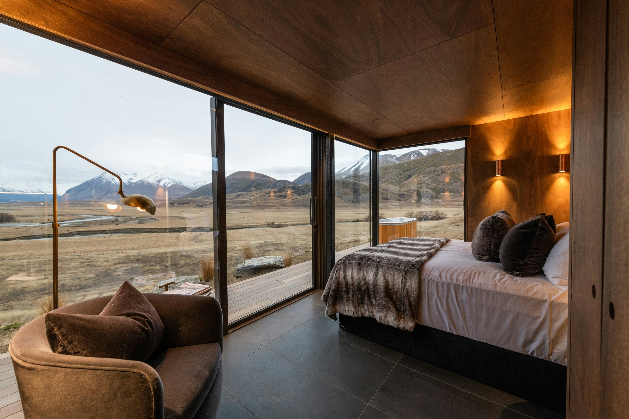 A king-sized bed and glass wall overlooking the forest in a Lindis Pod