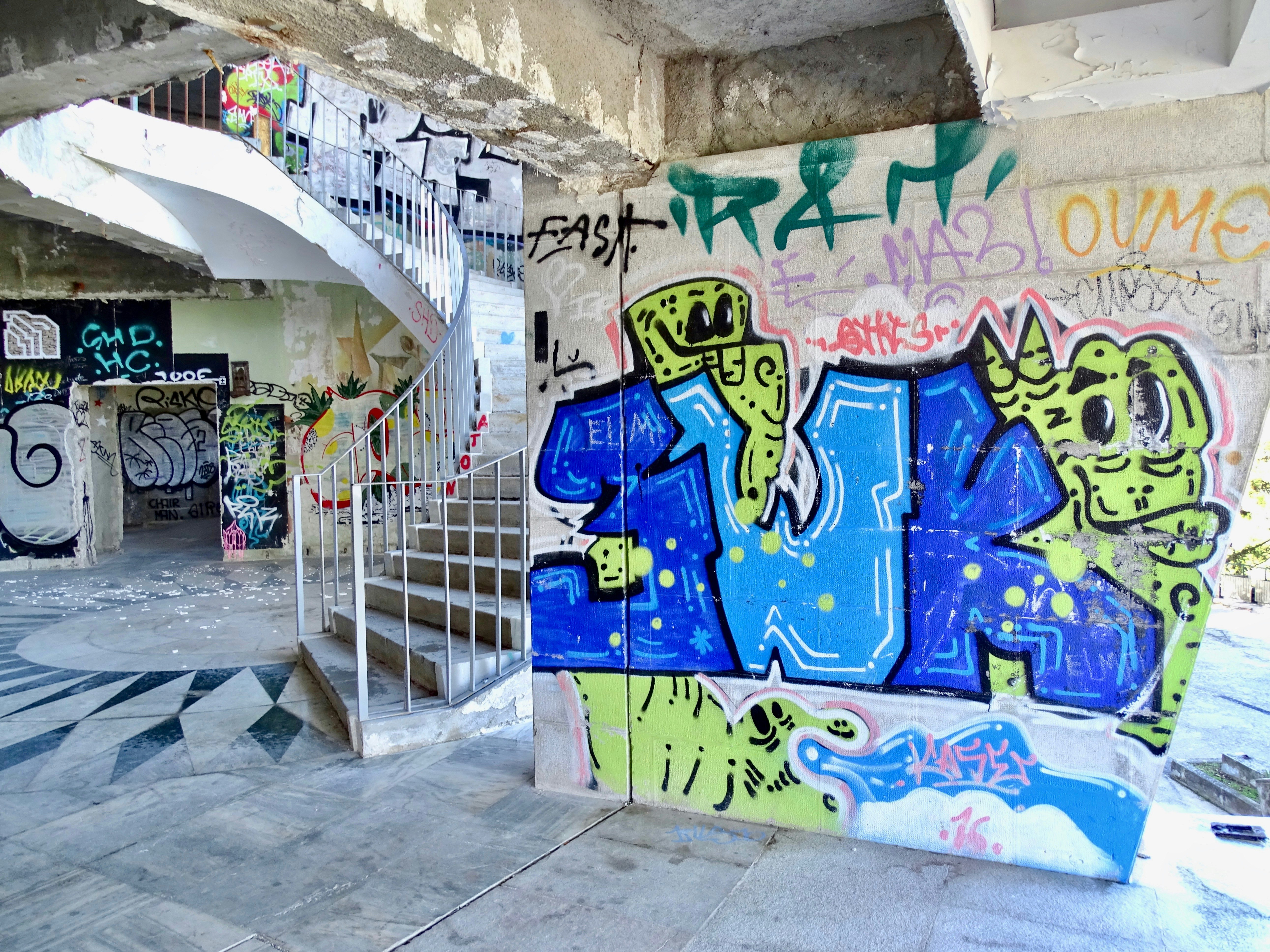 A concrete spiral staircase bordered by graffitied walls in the Miradouro Panoramico de Monsanto, Lisbon.
