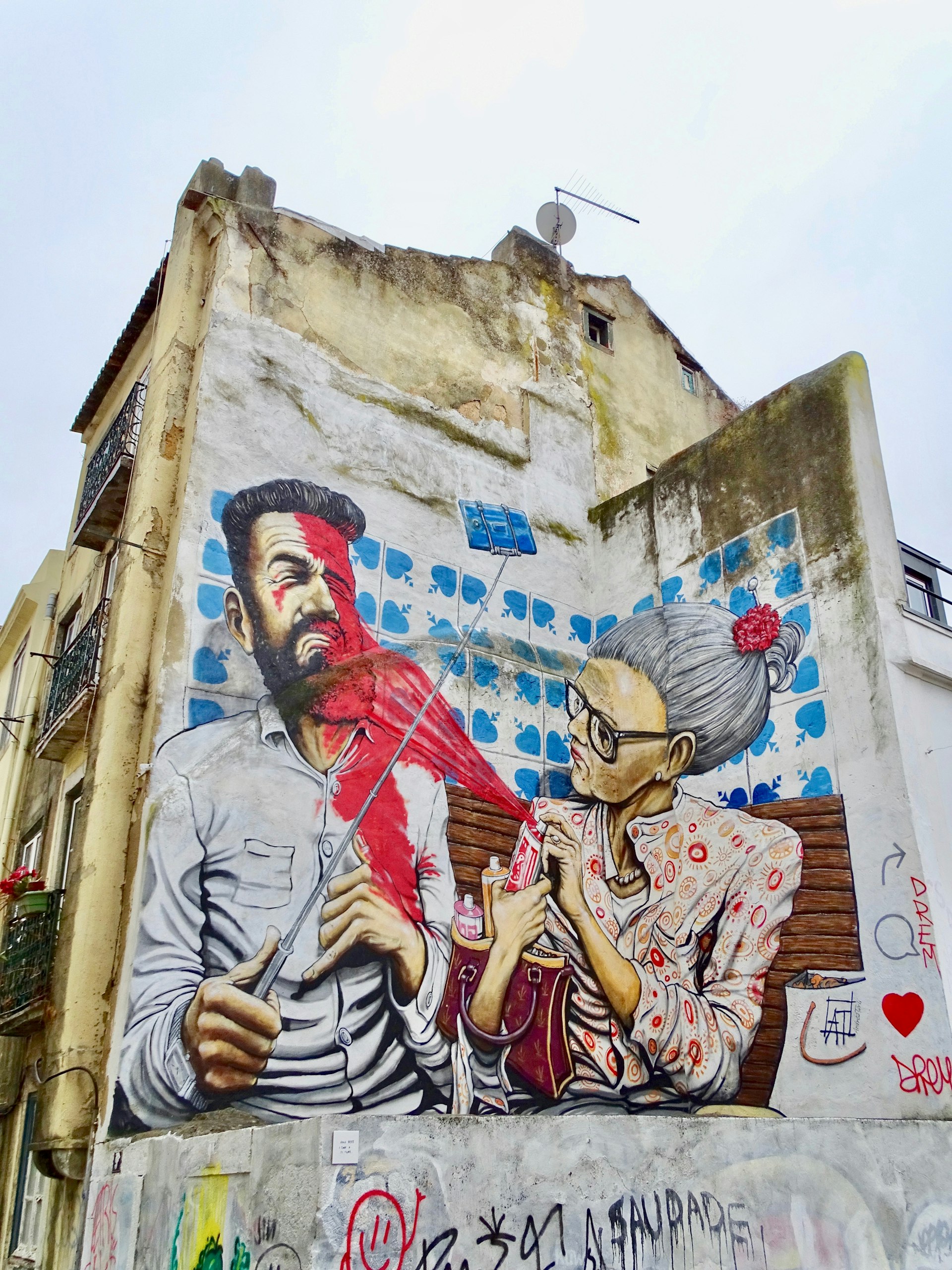 A mural along Largo Achada in Lisbon, portraying an older woman spraying the artist, caught mid-selfie, with a can of spray paint.