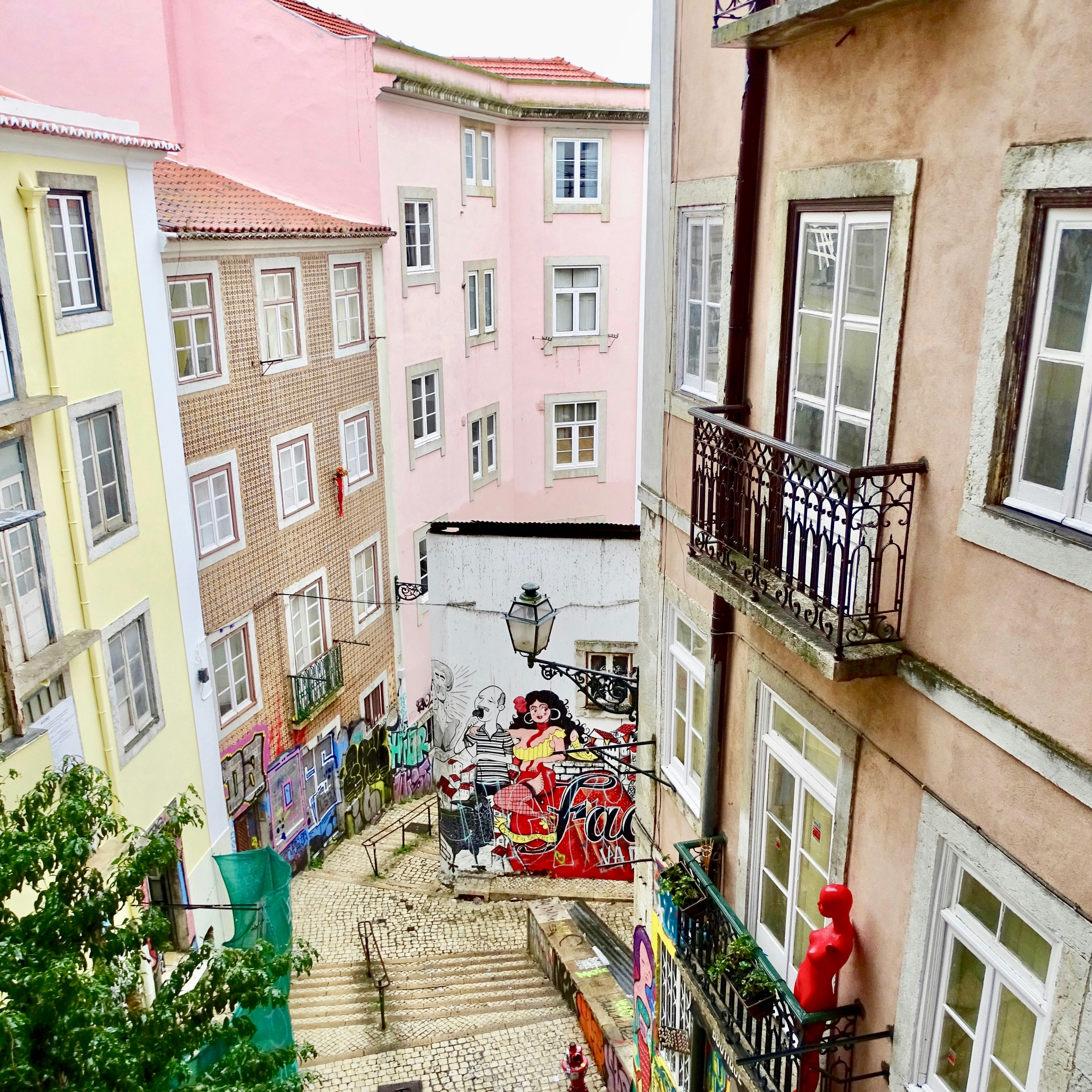 A view down a Lisbon alleyway with colourful buildings and a mural on the far wall.