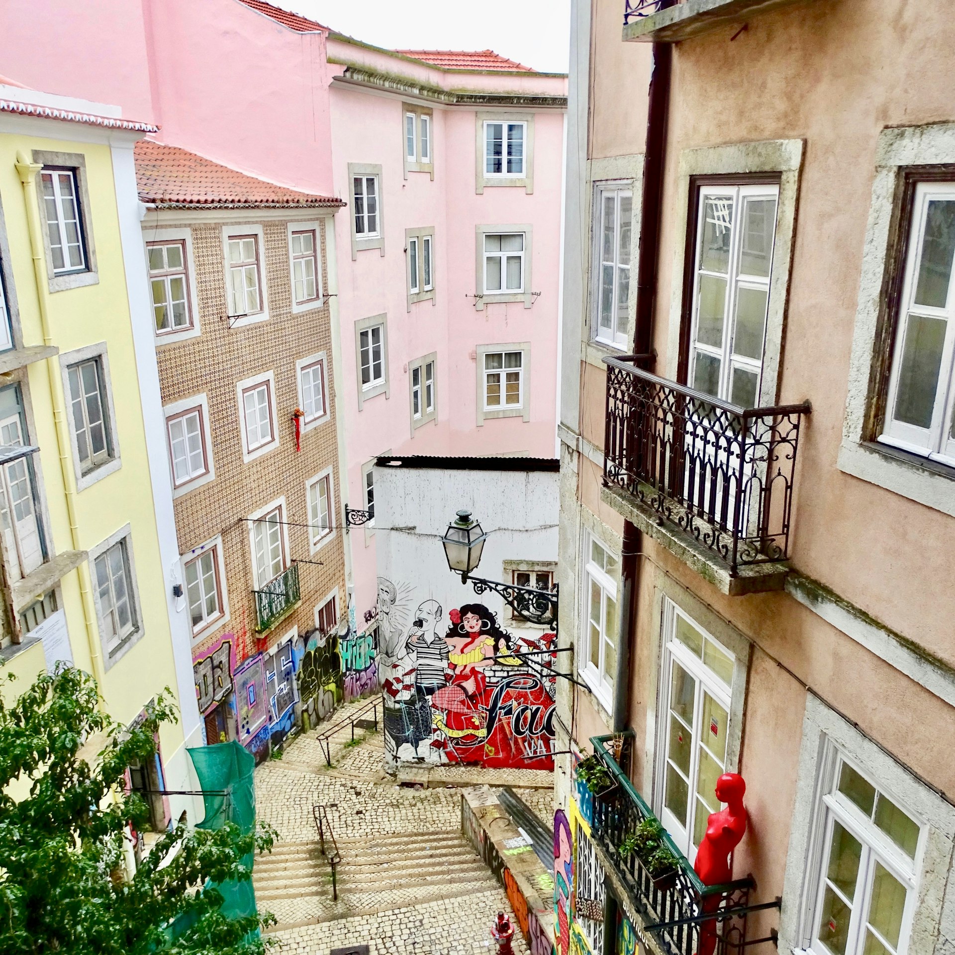 A view down a Lisbon alleyway with colourful buildings and a mural on the far wall.