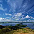Looking down a hillside towards Loch Lomond, dotted with verdant green islands, with a big sky full of wispy clouds overhead.