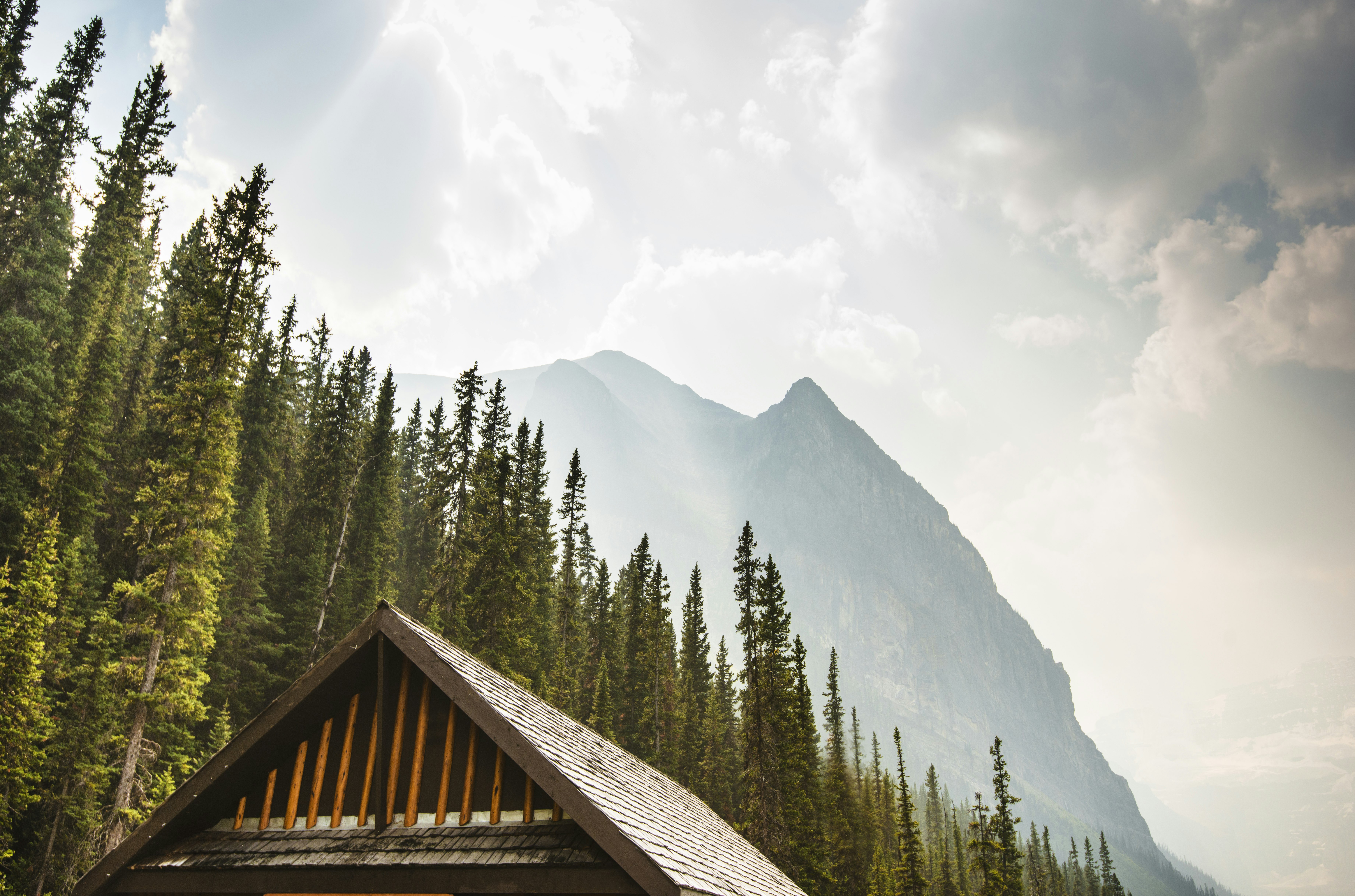 Just the roof of a rustic lodge is seen in the foreground as evergreen trees and snow covered mountains rise in the background; Banff and Jasper Backcountry Lodges