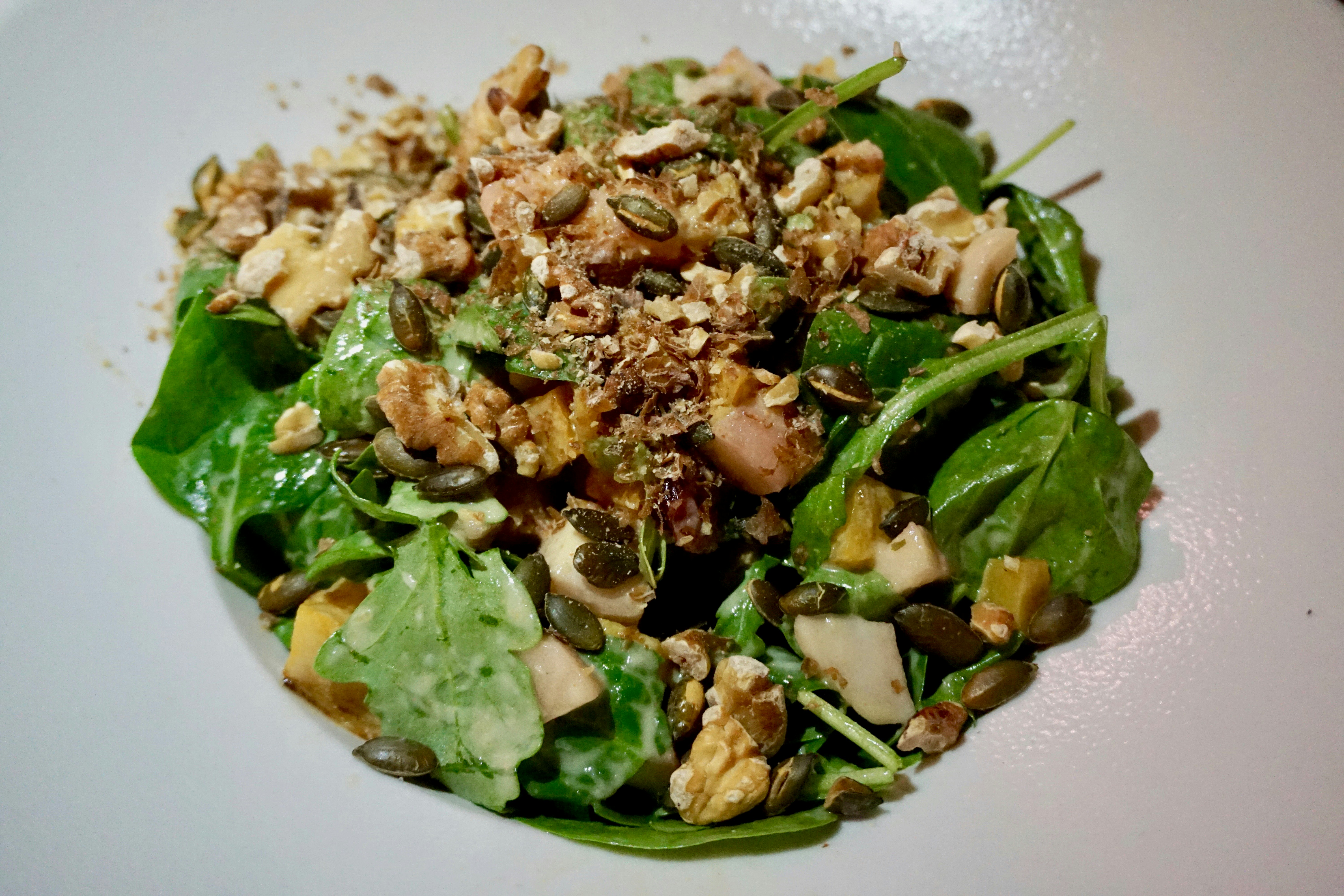Salad ingerdients including lettuce leaves, sunflower seeds and walnuts have been artfully arranged on a white plate.