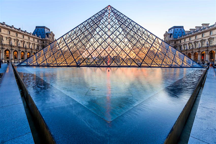 Louvre - Paris Highlights.jpg The glass pyramid of the Louvre at dusk, with its fountain in front and the ornate facades of the museum building on either side.