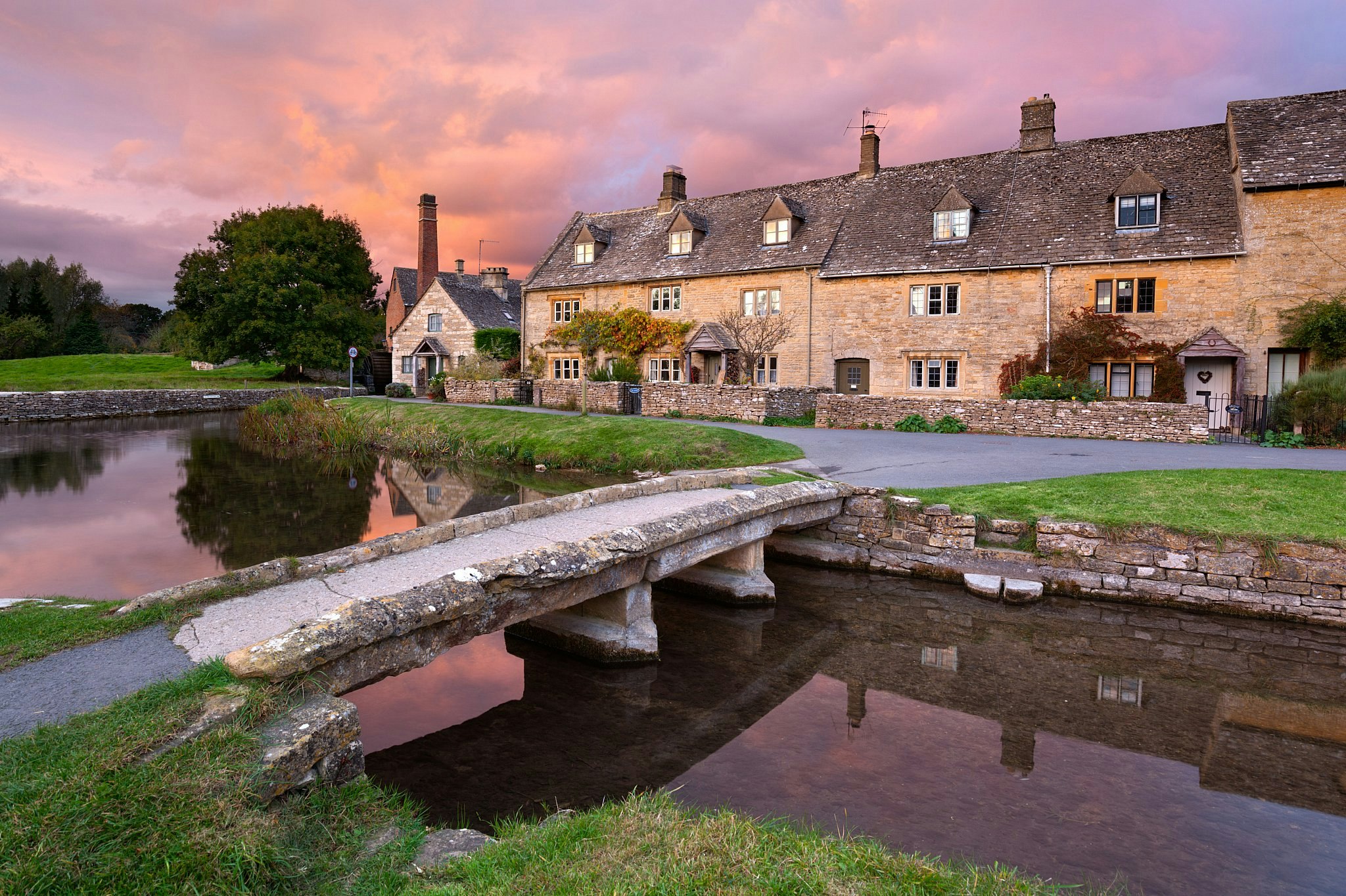 A small stone bridge crossing a river to a row of stone cottages at sunset.
