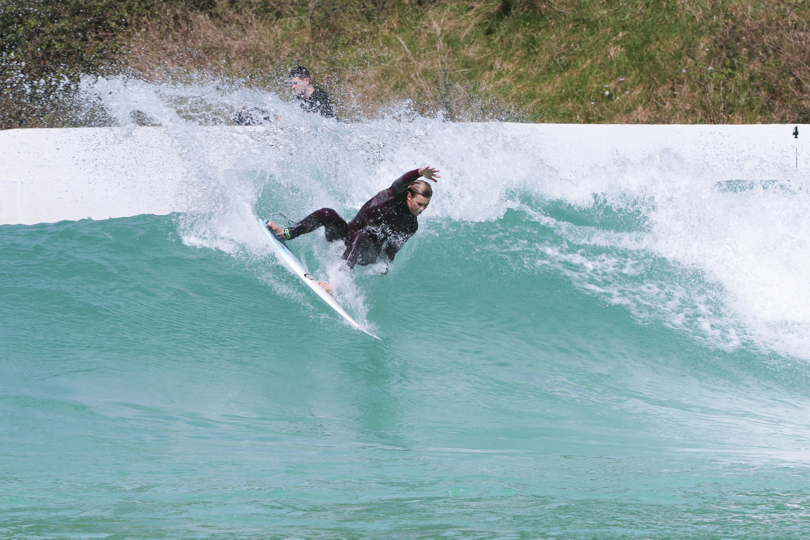 A female surfer in a black wetside rides a wave in an artificial lagoon