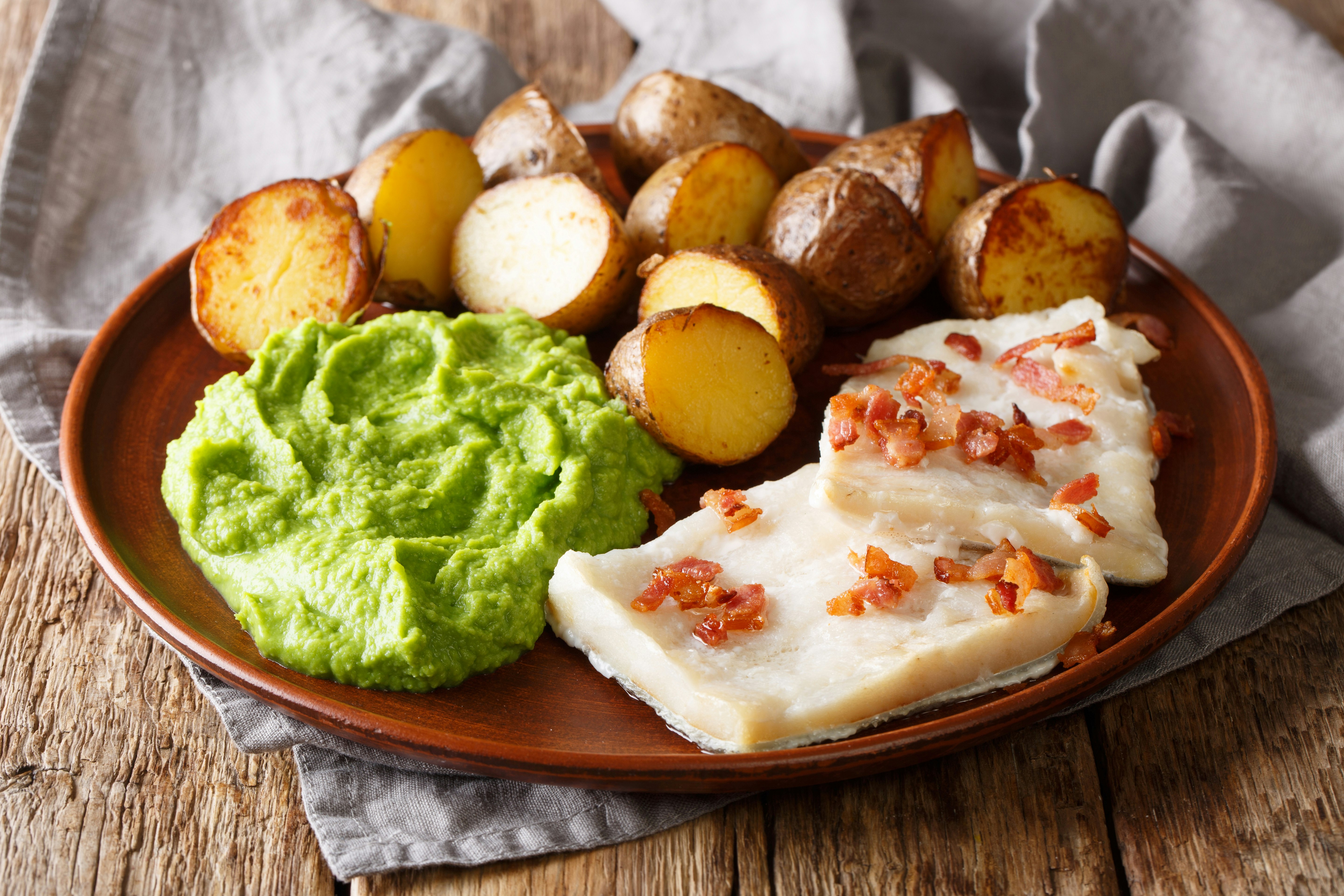 Traditional Scandinavian dish of lutefisk topped with bacon bits, pea puree and potatoes 