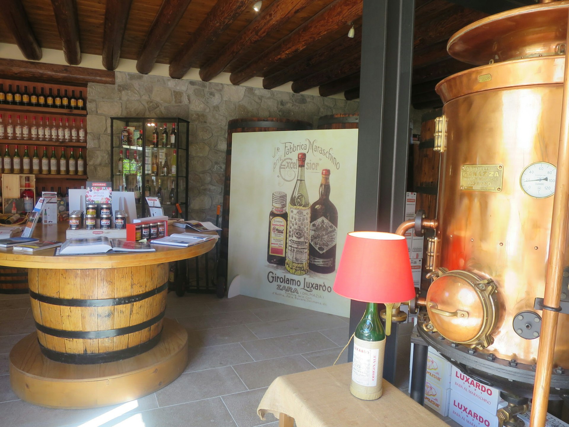 The Luxardo shop inside a former farmhouse. A large copper still is on the right with products displayed on a huge barrel turned into a table and shelves on the right-hand side