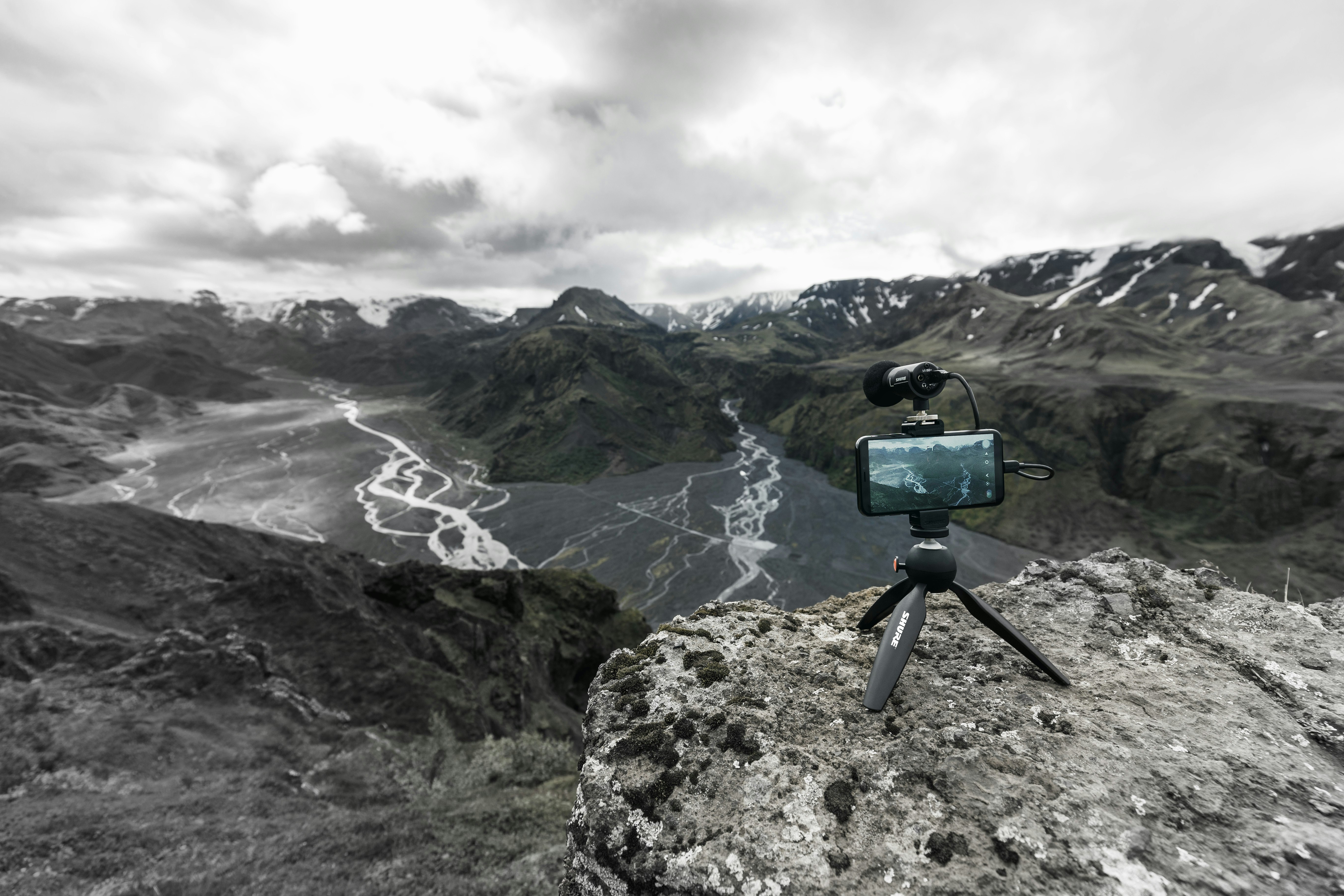 A smartphone on a tripod set up on a cliff overlooking a deep valley, with gray clouds overhead