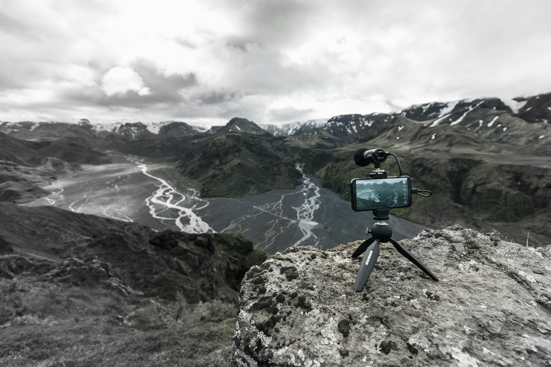 A smartphone on a tripod set up on a cliff overlooking a deep valley, with gray clouds overhead